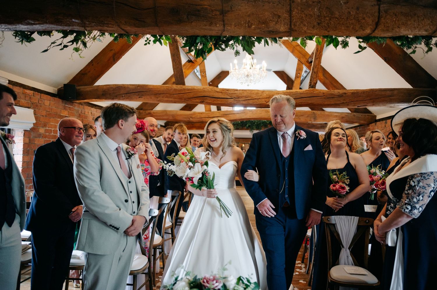 A wedding ceremony takes place in a rustic barn venue with exposed wooden beams and brick walls.