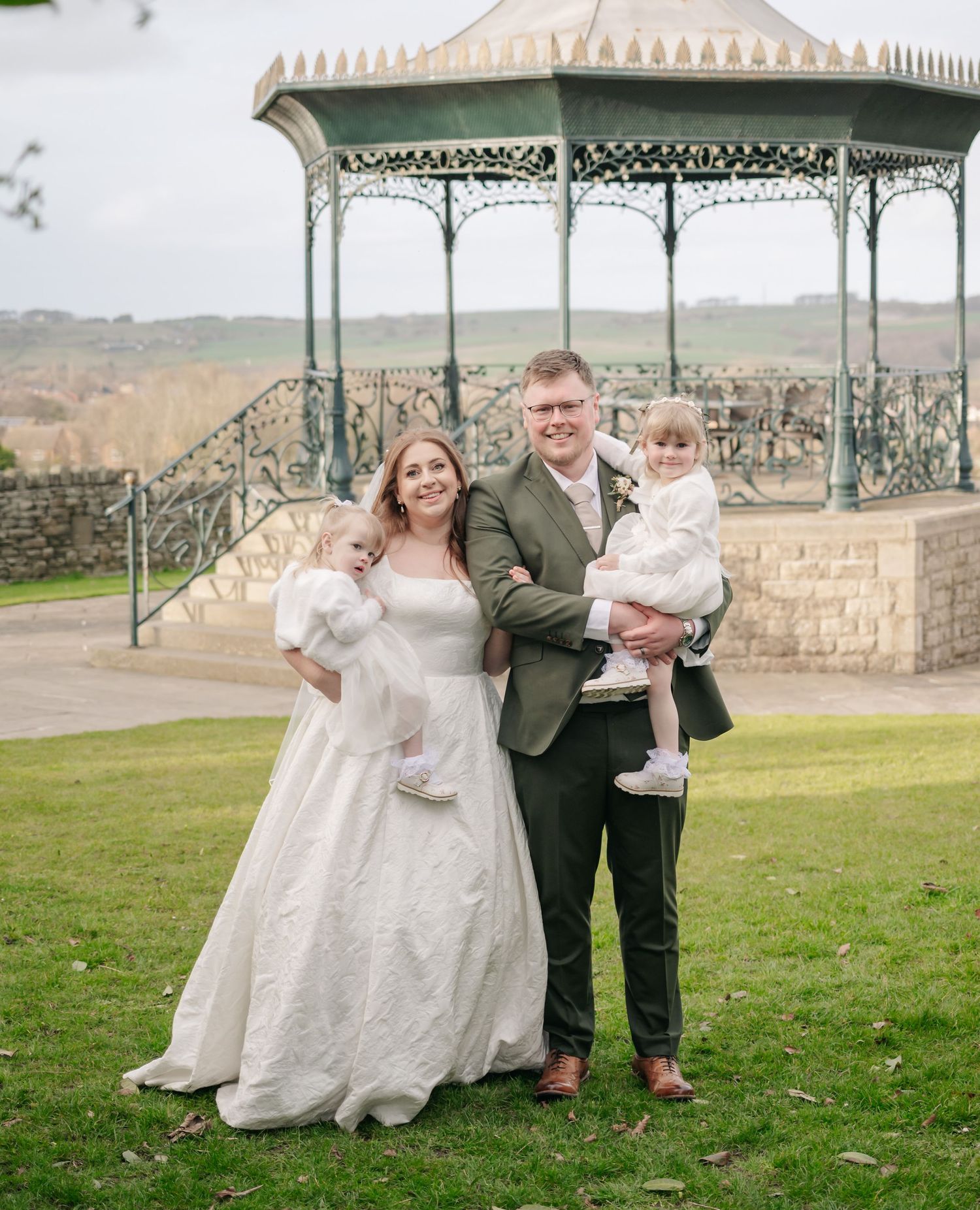 A couple poses for photos under an ornate Victorian-style gazebo in a garden setting.