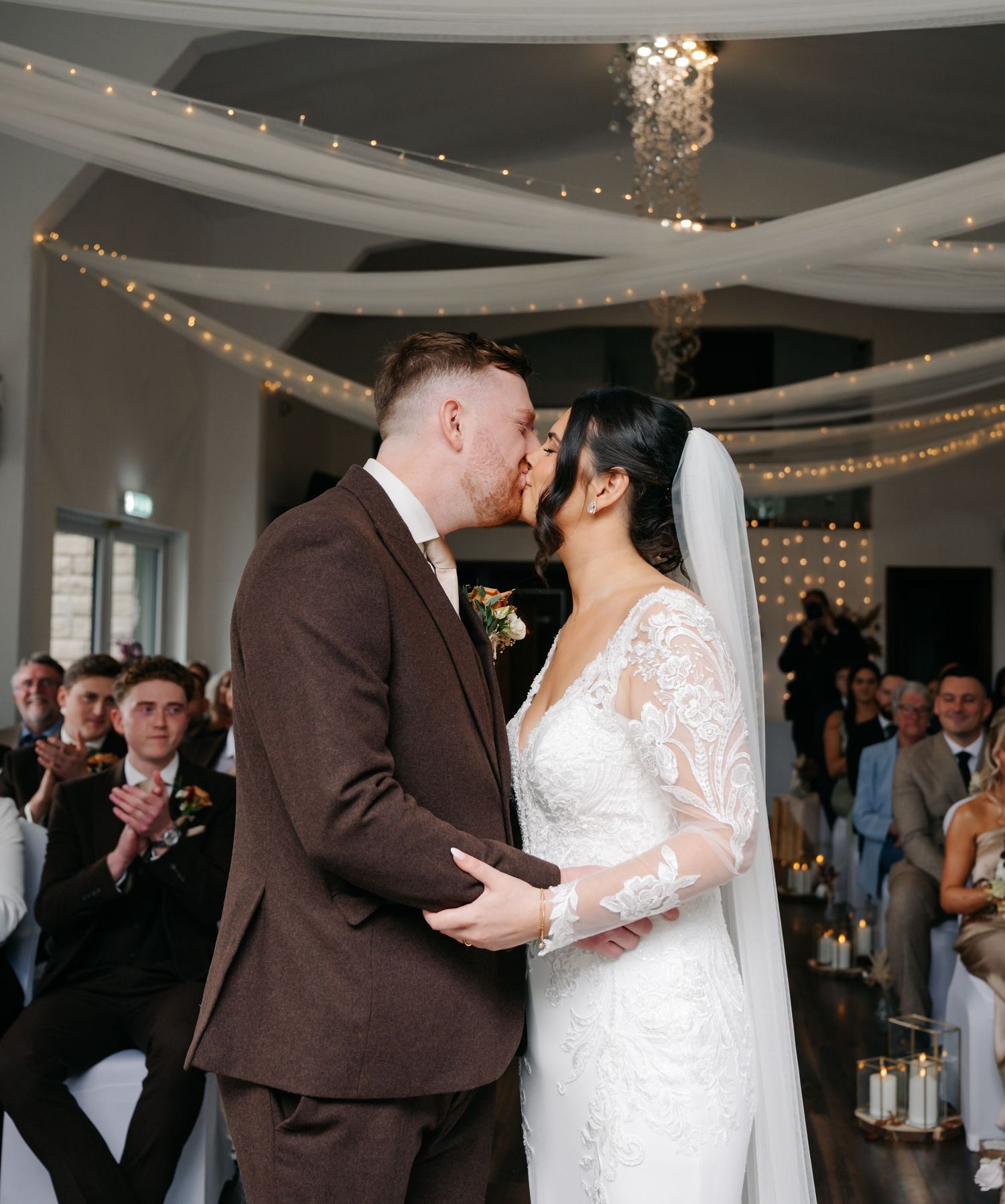 A wedding reception in an elegant venue with string lights and guests celebrating the newlyweds.