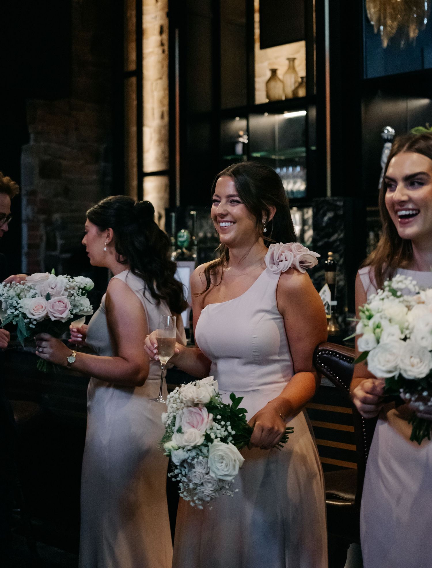Wedding party members in light pink dresses share laughs and drinks during reception celebrations.