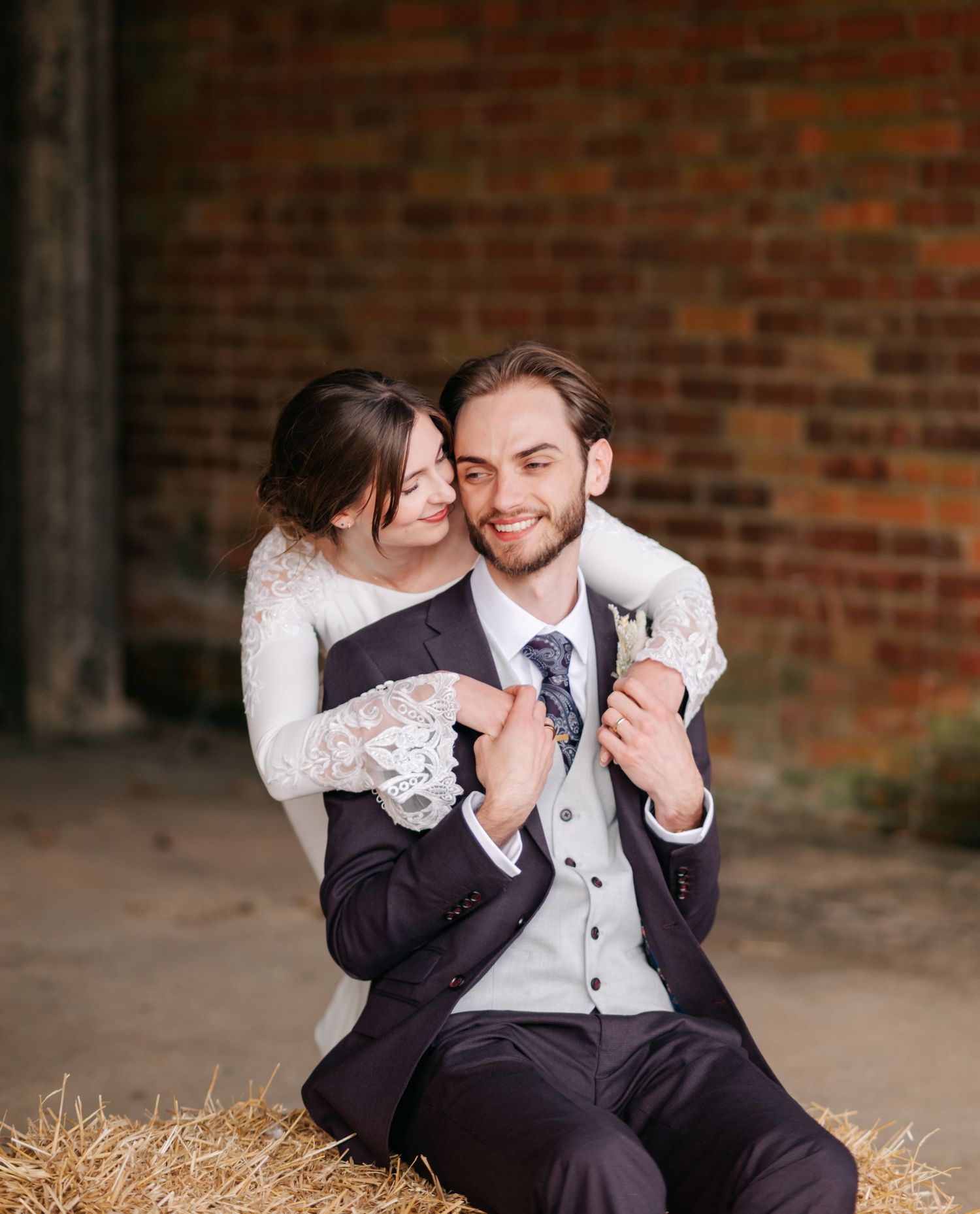A couple shares an intimate moment while sitting on hay bales against a brick wall backdrop.