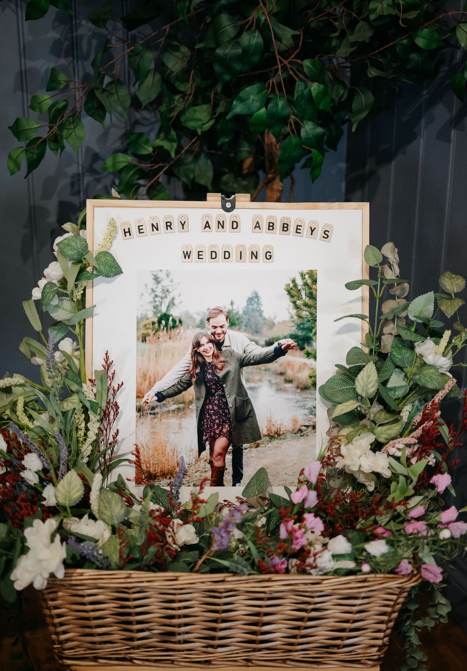 A wedding photo display in a wicker basket surrounded by fresh flowers and greenery.
