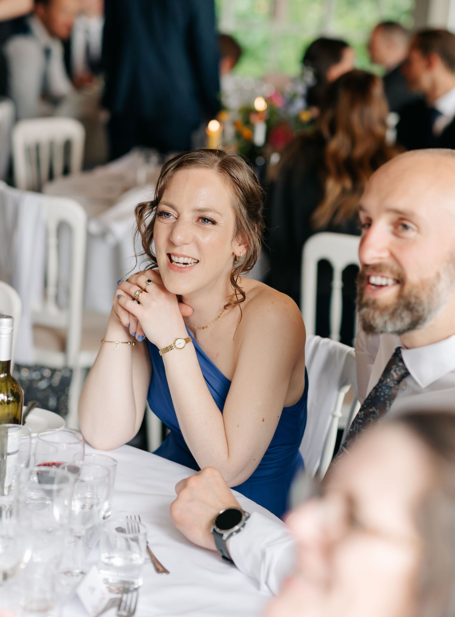 Wedding reception guests share animated conversations and laughs at formal dinner table settings.