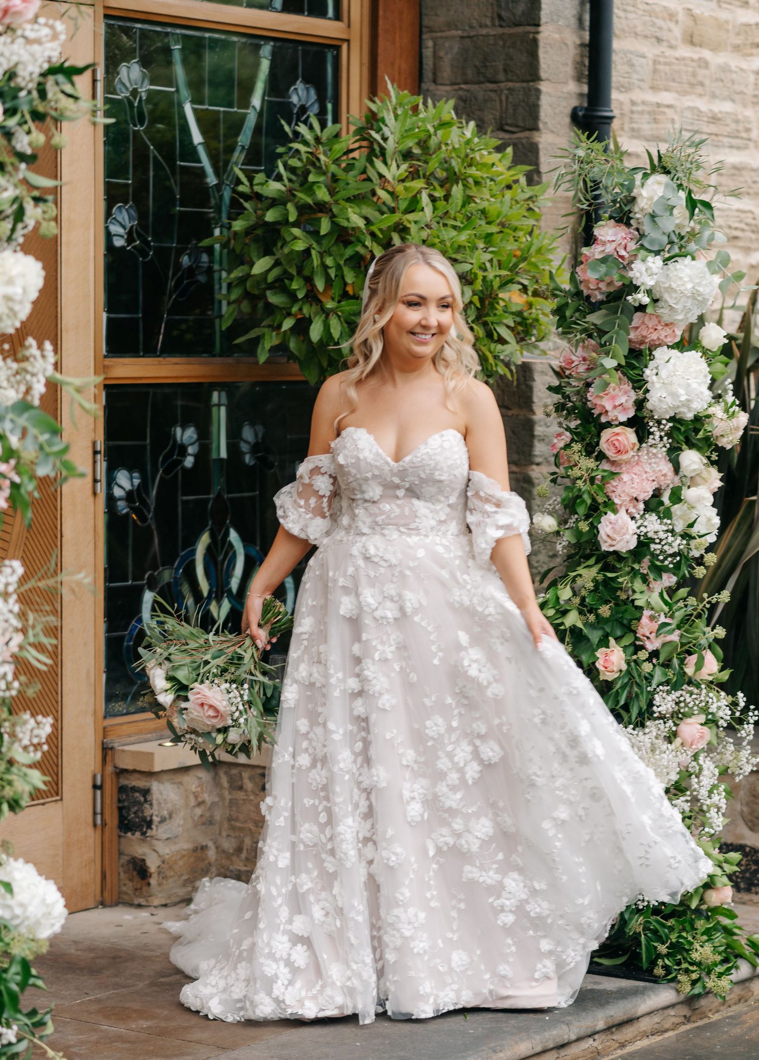 Bride in floral applique wedding gown poses in garden setting with blooming roses.