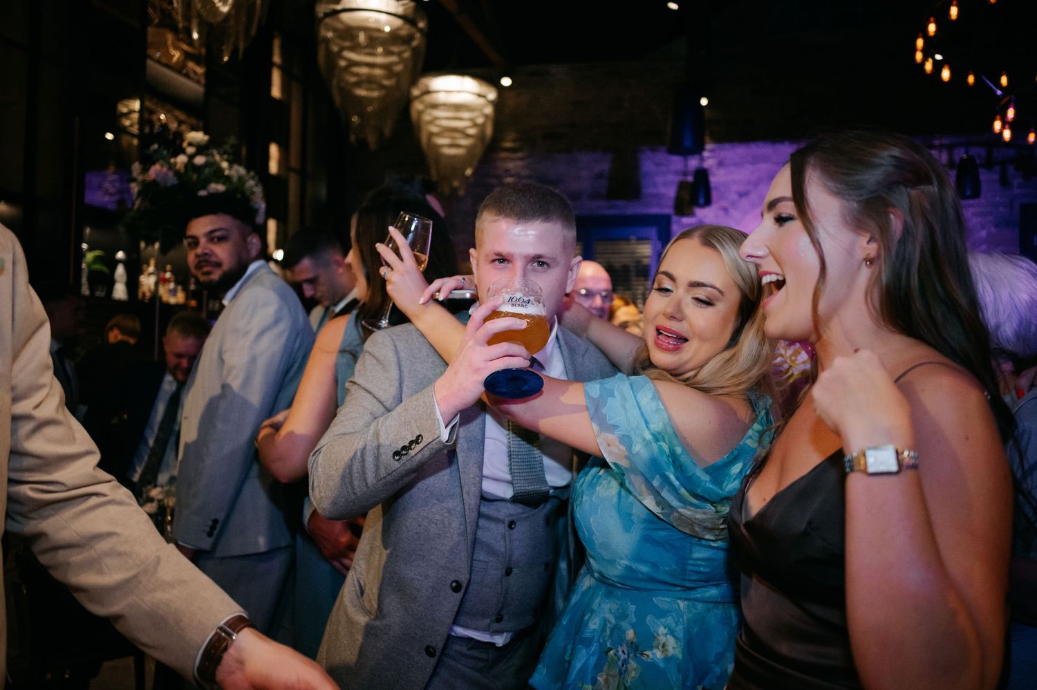 Guests enjoying themselves on a lively dance floor at an evening wedding reception with purple lighting.