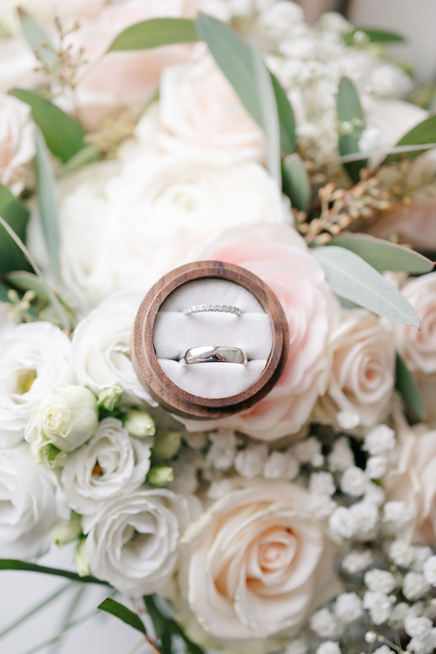 Wedding rings nestled among delicate pink and white roses with baby's breath flowers.