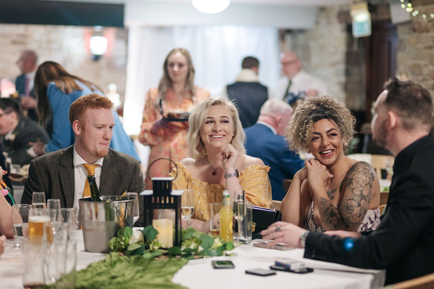 Wedding guests gathered around elegant dining tables during a reception celebration at an indoor venue.