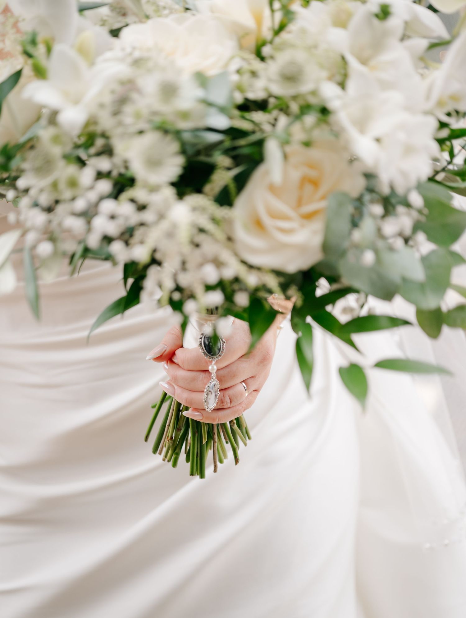 Elegant white wedding bouquet with roses and greenery against white fabric.
