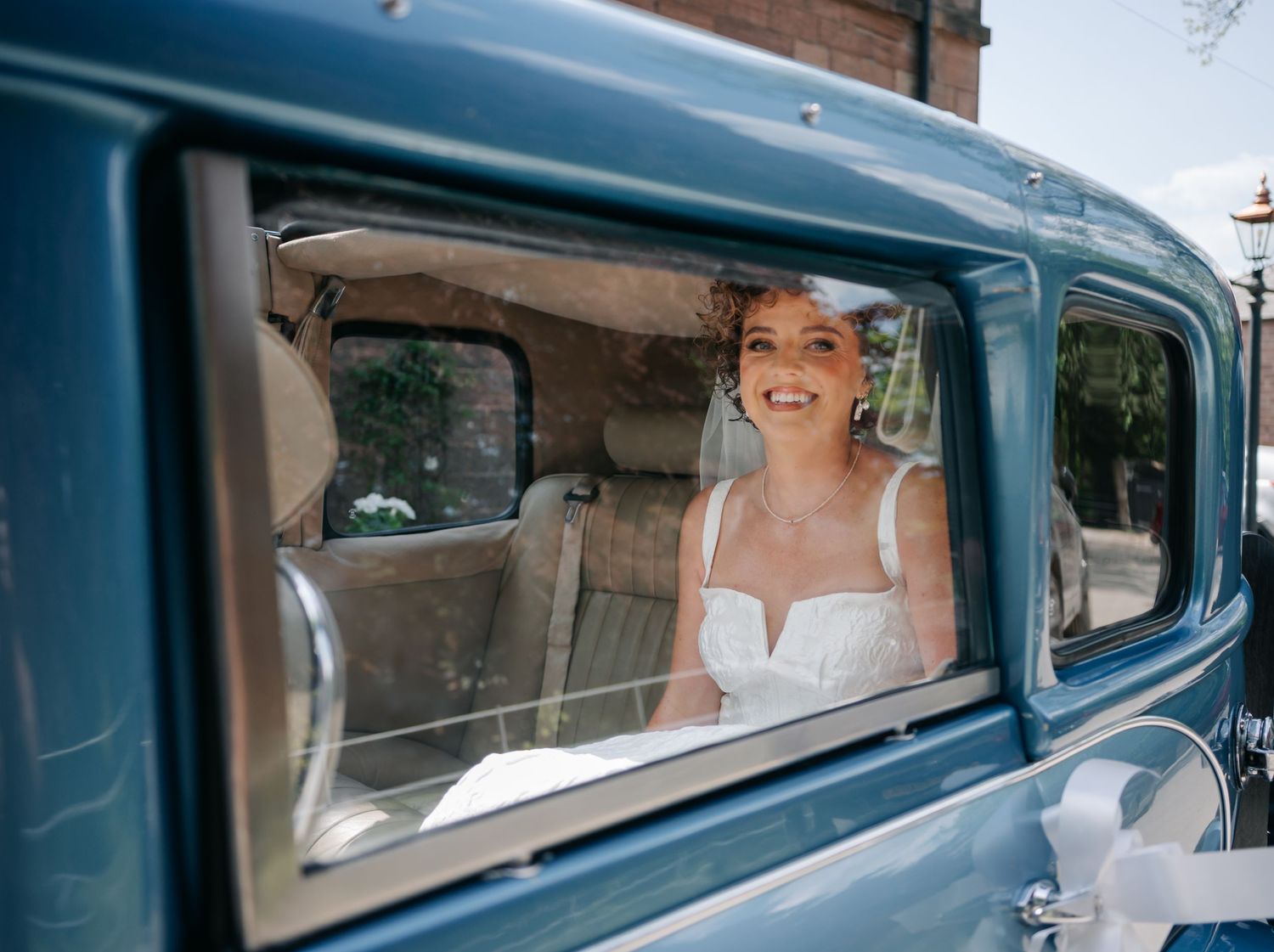 A vintage blue classic car with passengers inside seen through multiple window frames.