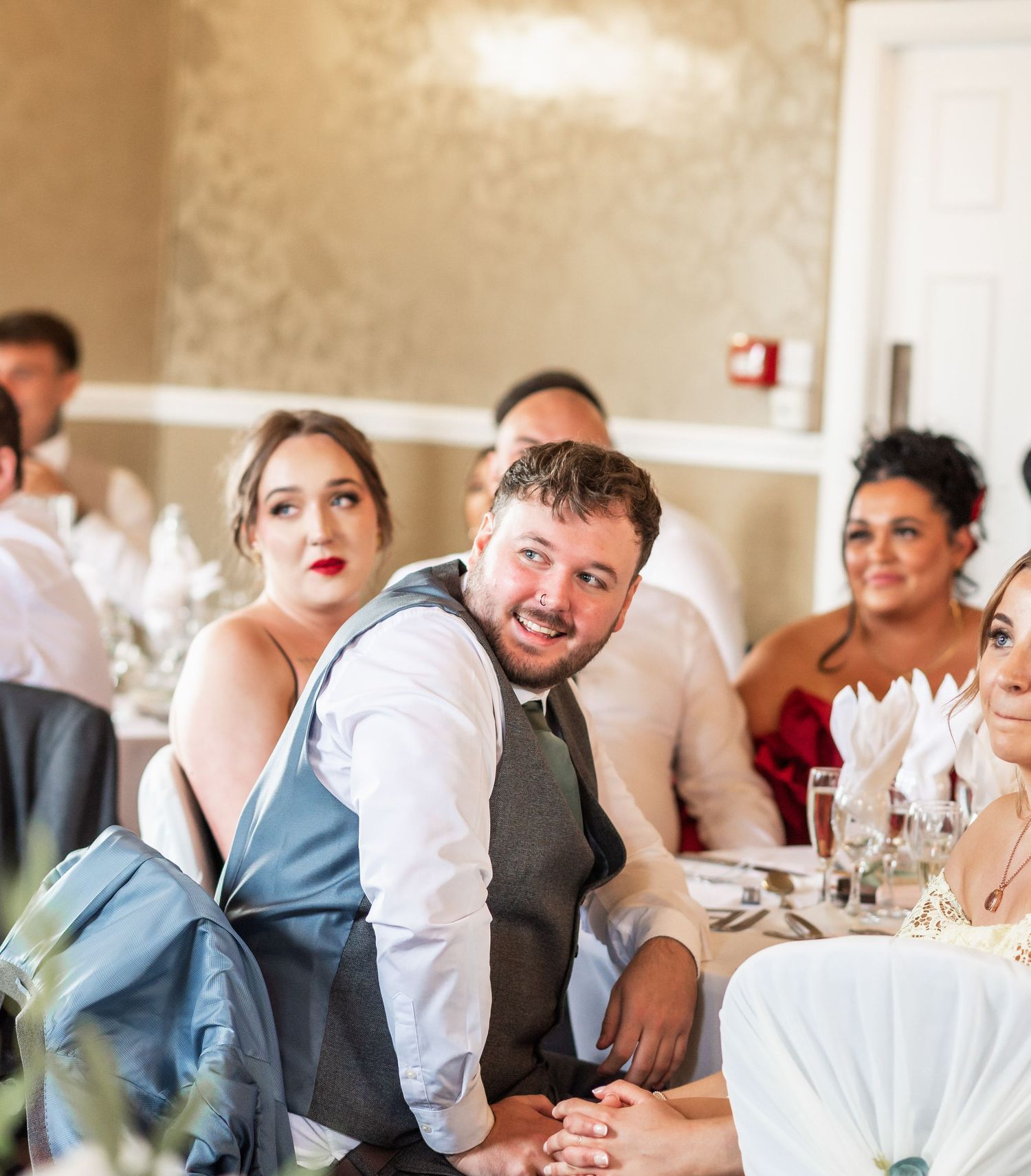 Wedding reception guests smile and laugh while seated at decorated tables during a celebration.
