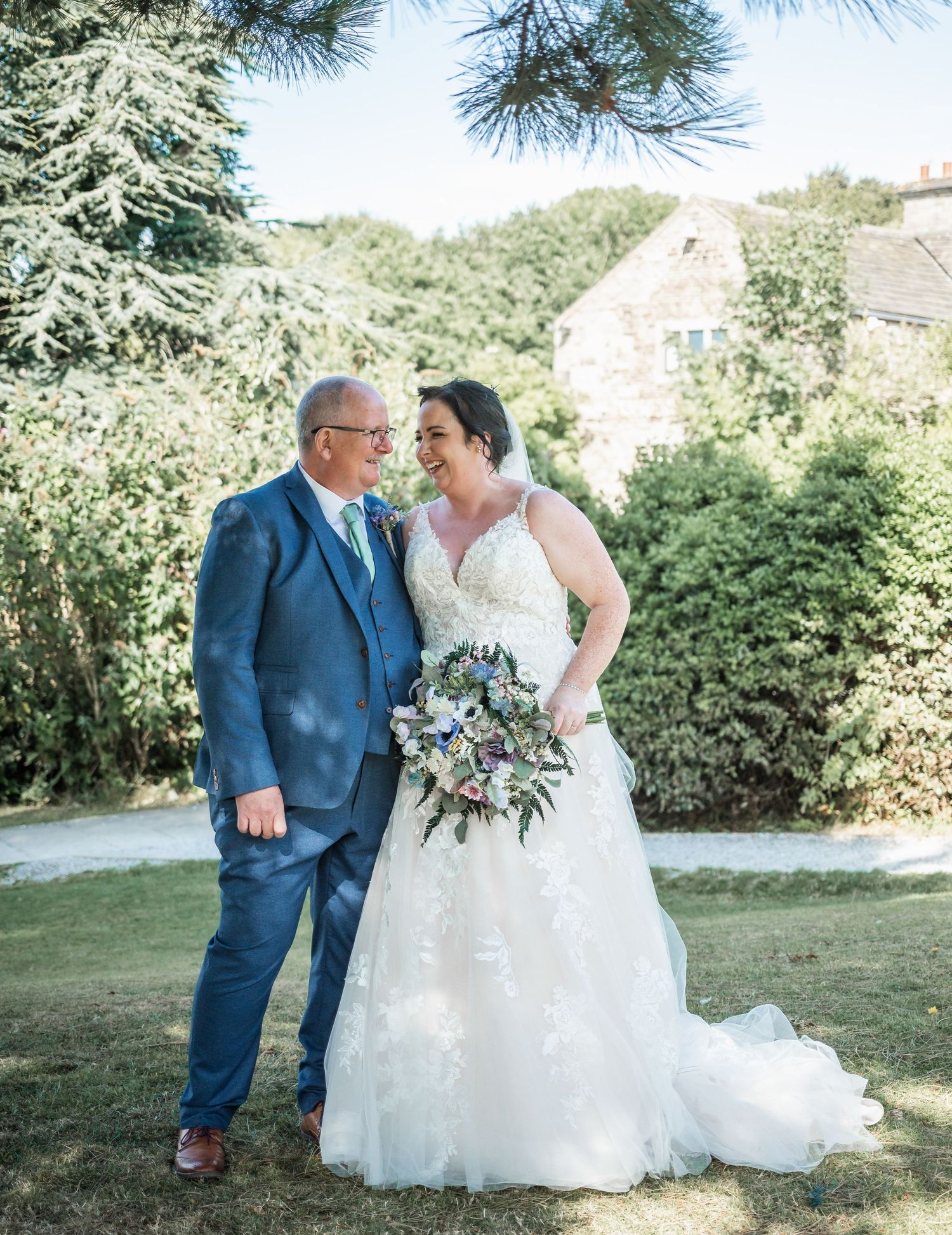 Elegant outdoor wedding portrait with stone building backdrop and lush gardens.