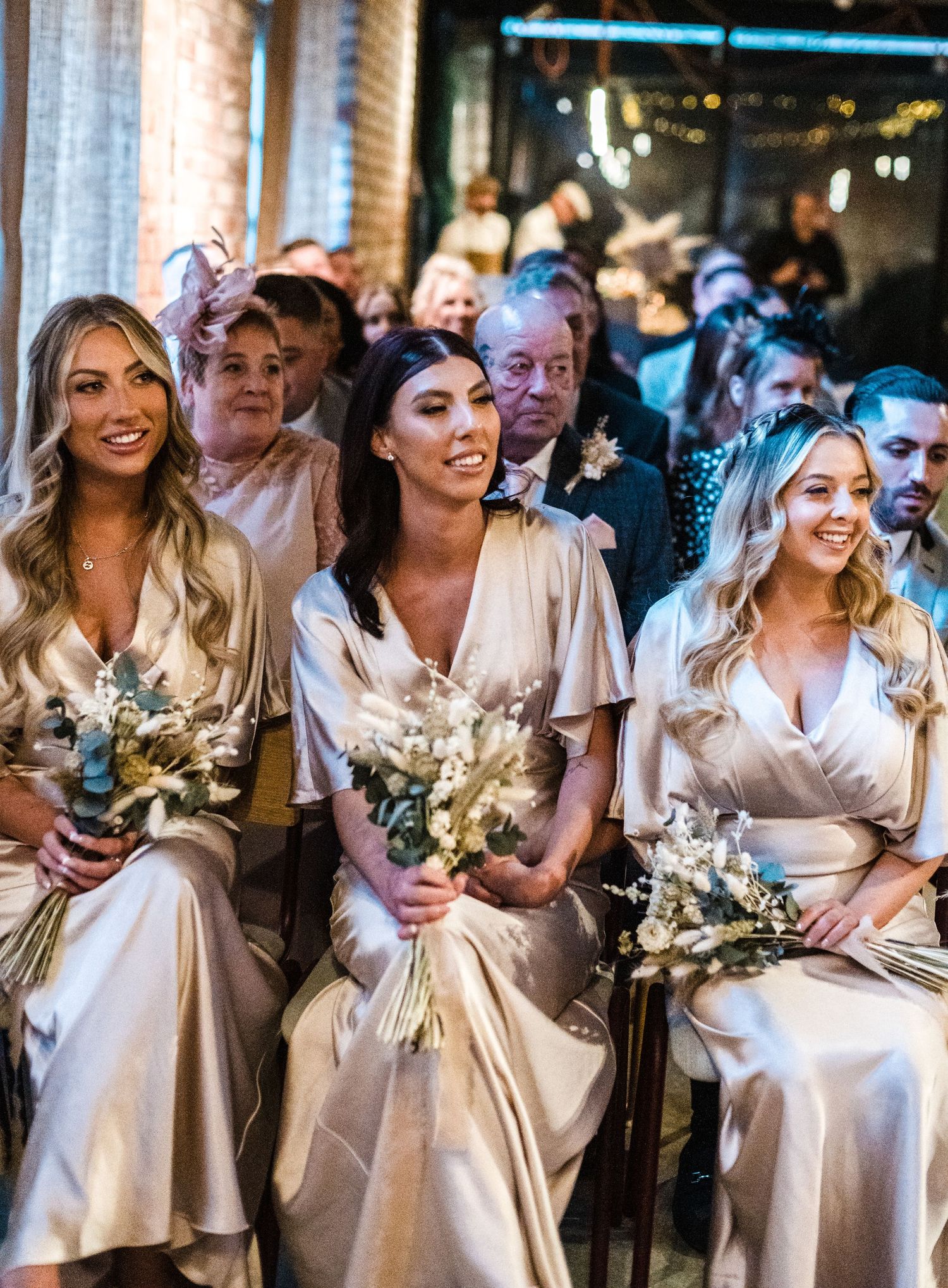 Bridesmaids in silk champagne dresses holding dried flower bouquets.