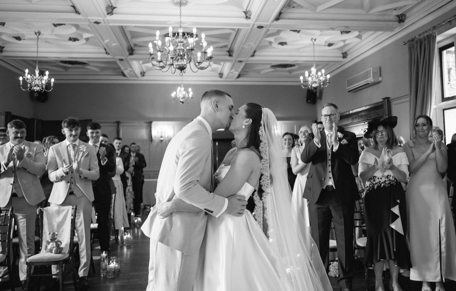Wedding reception venue with elegant white decor and chandeliers showing guests celebrating.