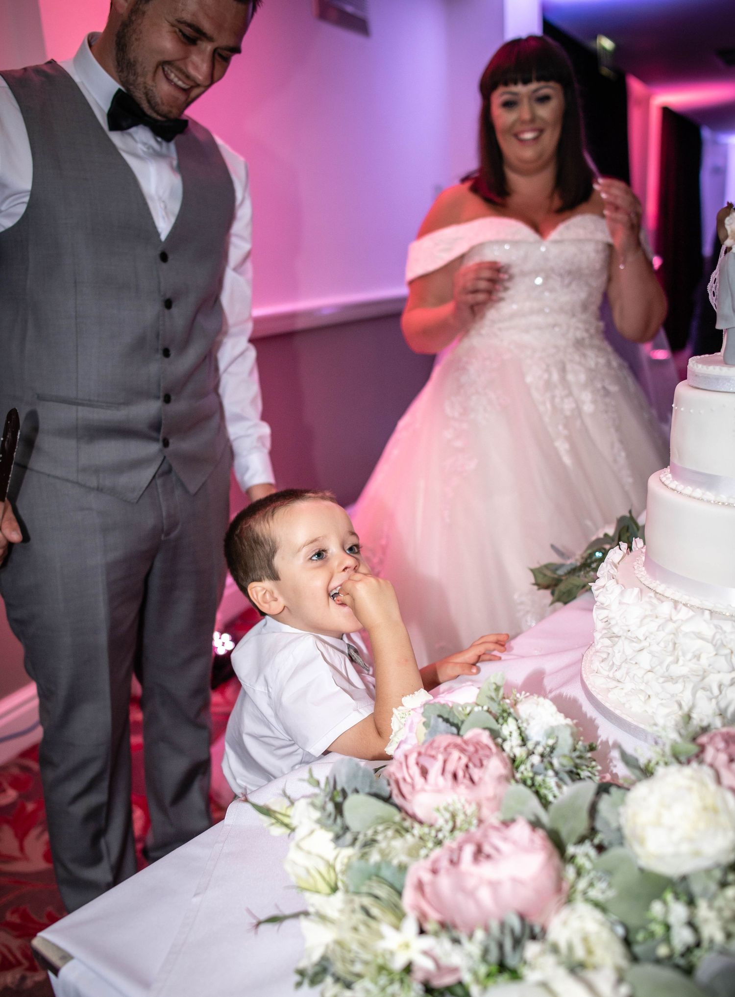 An intimate moment at a wedding reception featuring a white tiered cake with pink floral decorations.