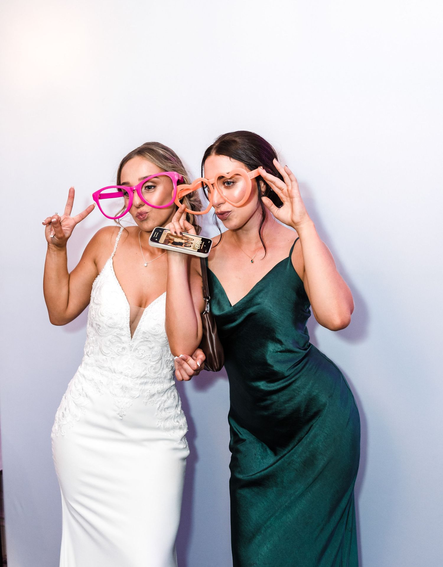 Two people posing with fun photo props against white background at wedding celebration.