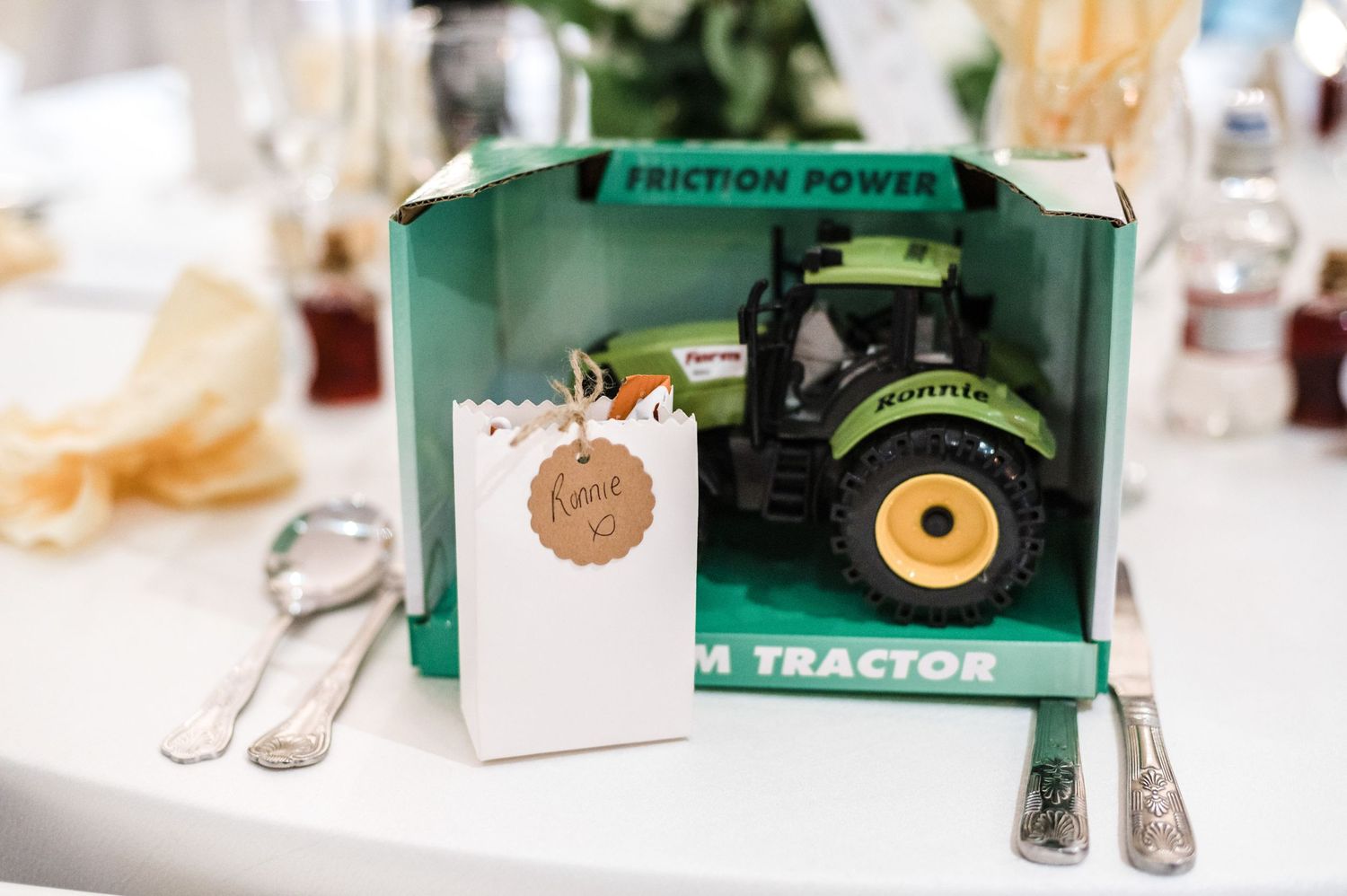 Green toy tractor display with place card at wedding reception table setting.