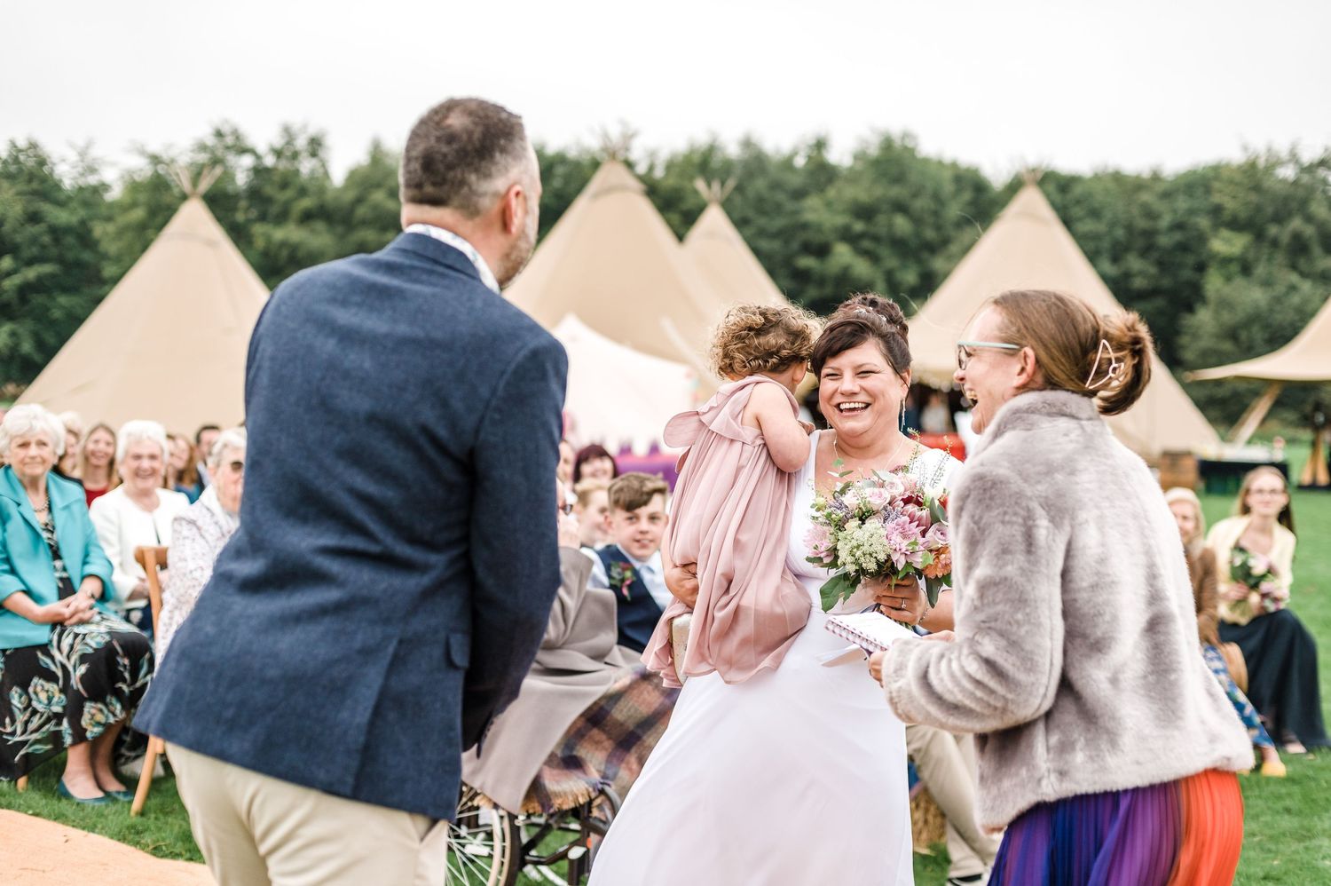 Outdoor wedding celebration with guests and tipi tents in background.