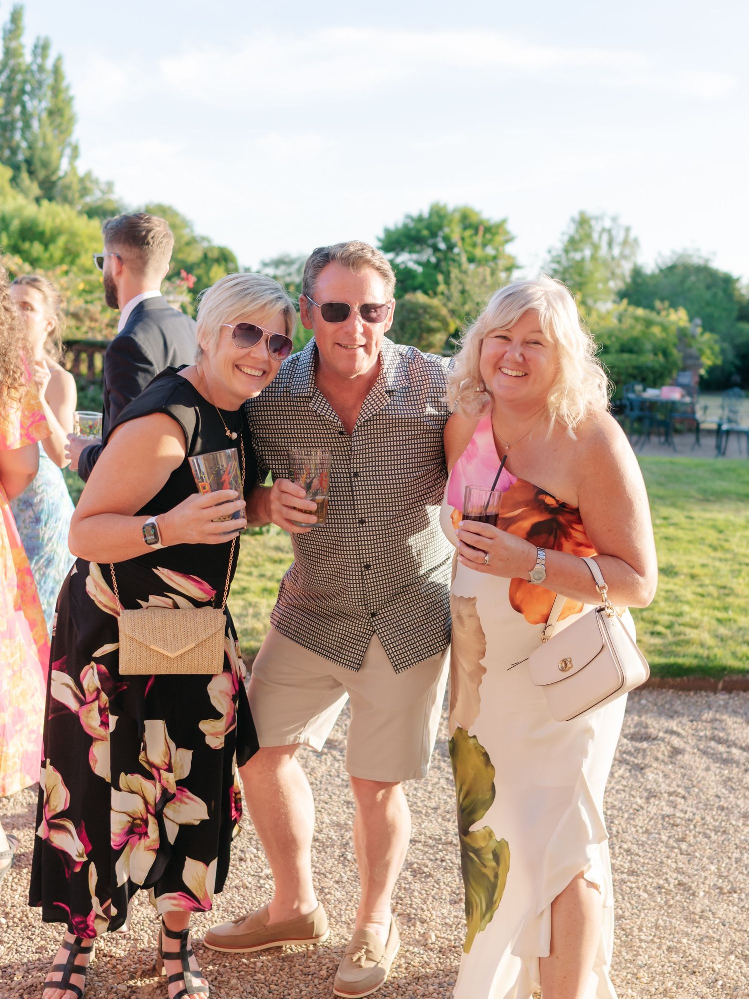 Wedding guests enjoying drinks and laughter at outdoor summer reception.