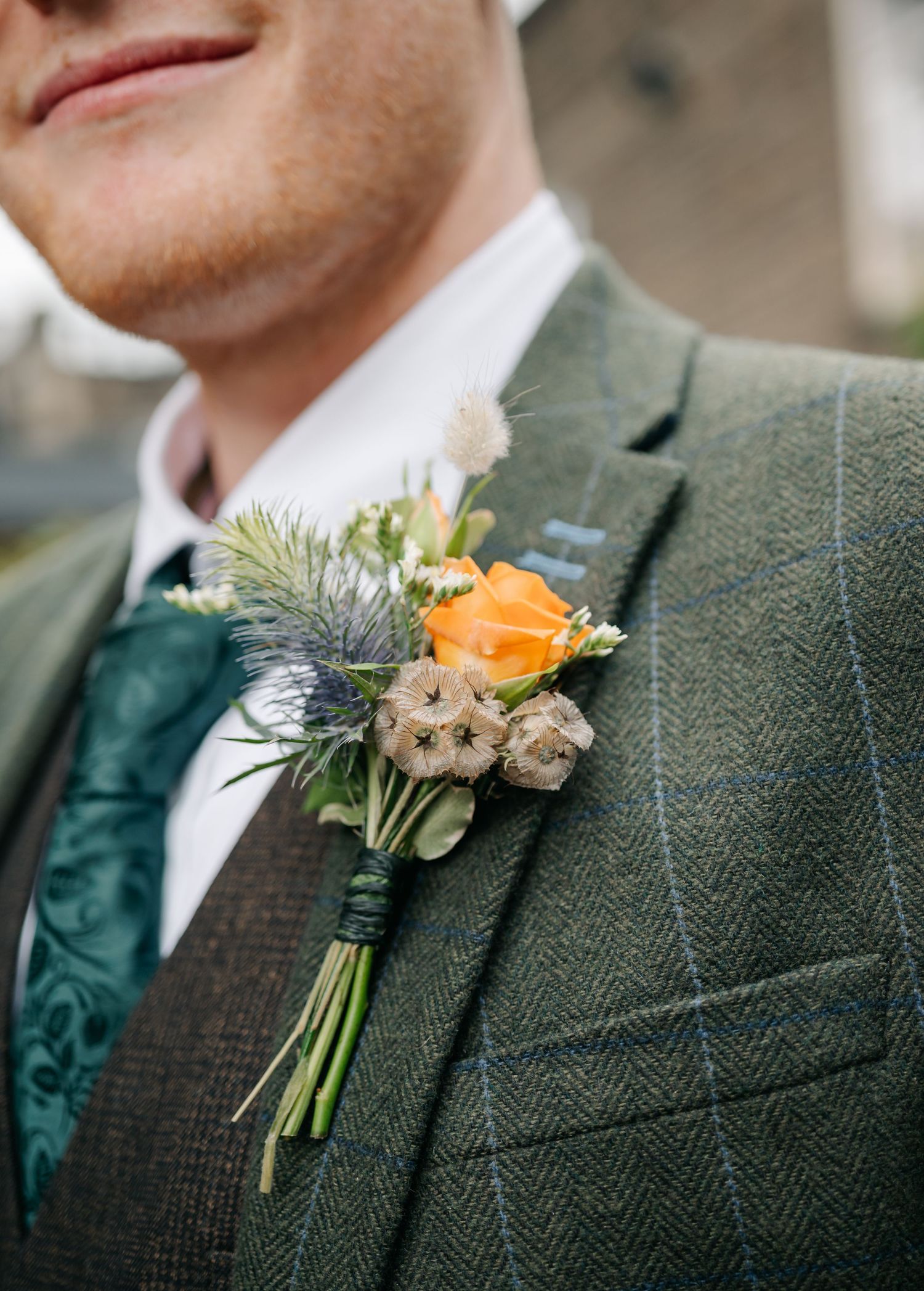 Close-up detail of green tweed suit jackets with floral boutonnieres in orange and cream colors.