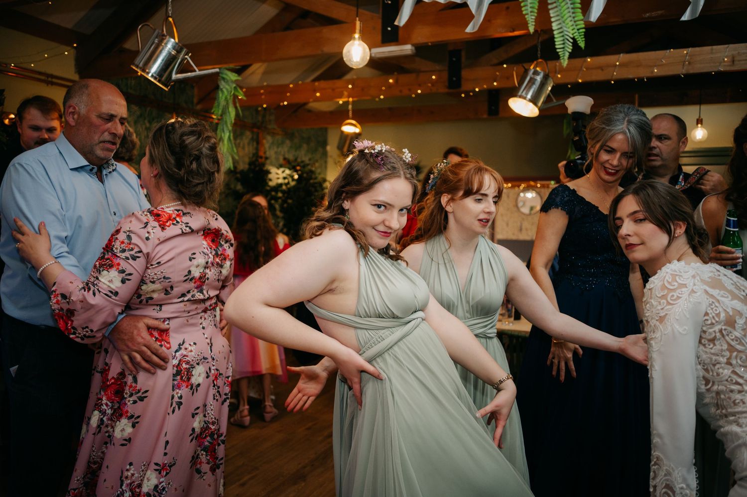 Wedding guests dancing and celebrating at a reception with string lights overhead.