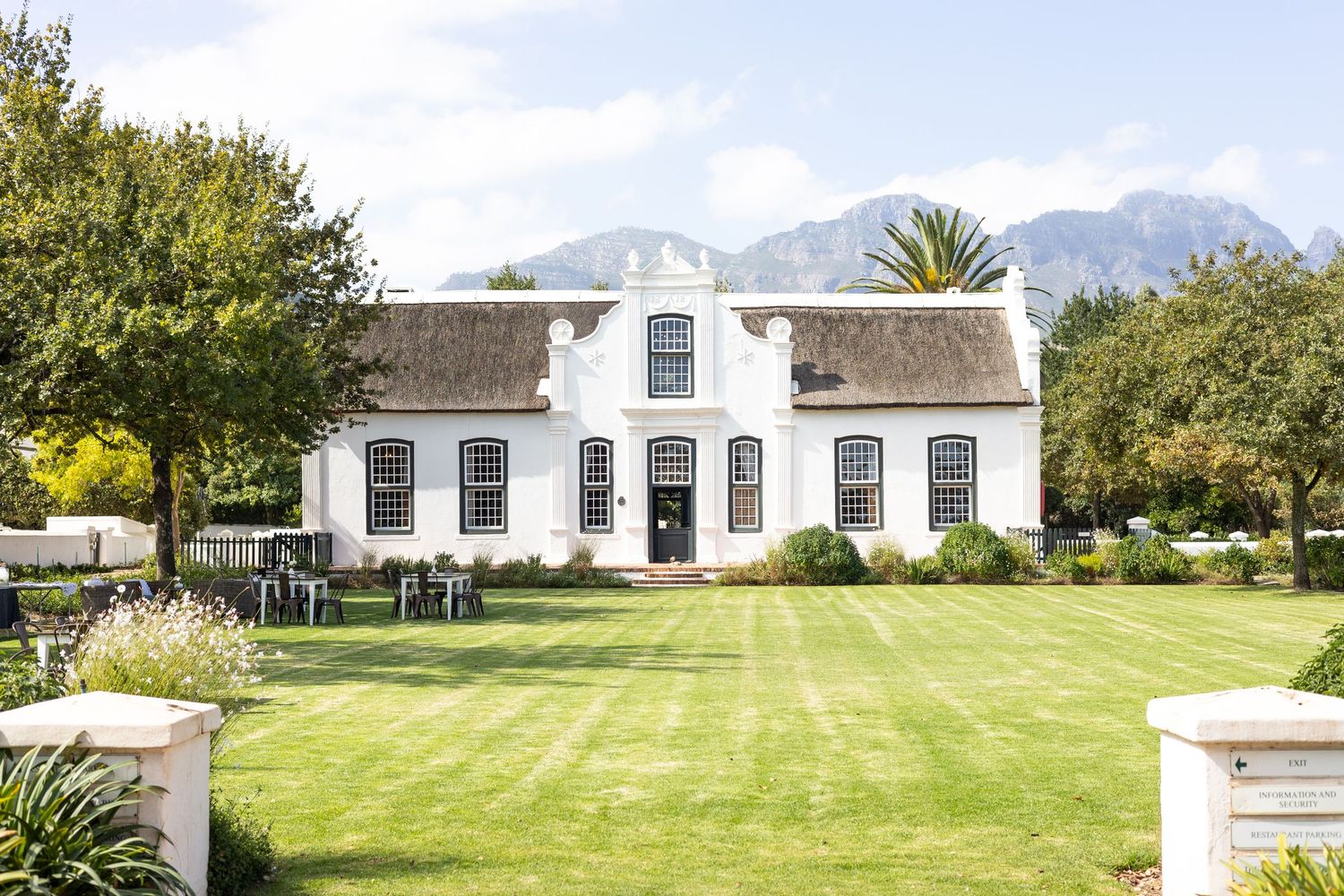 Cape Dutch style white manor house with manicured lawn and mountain backdrop.