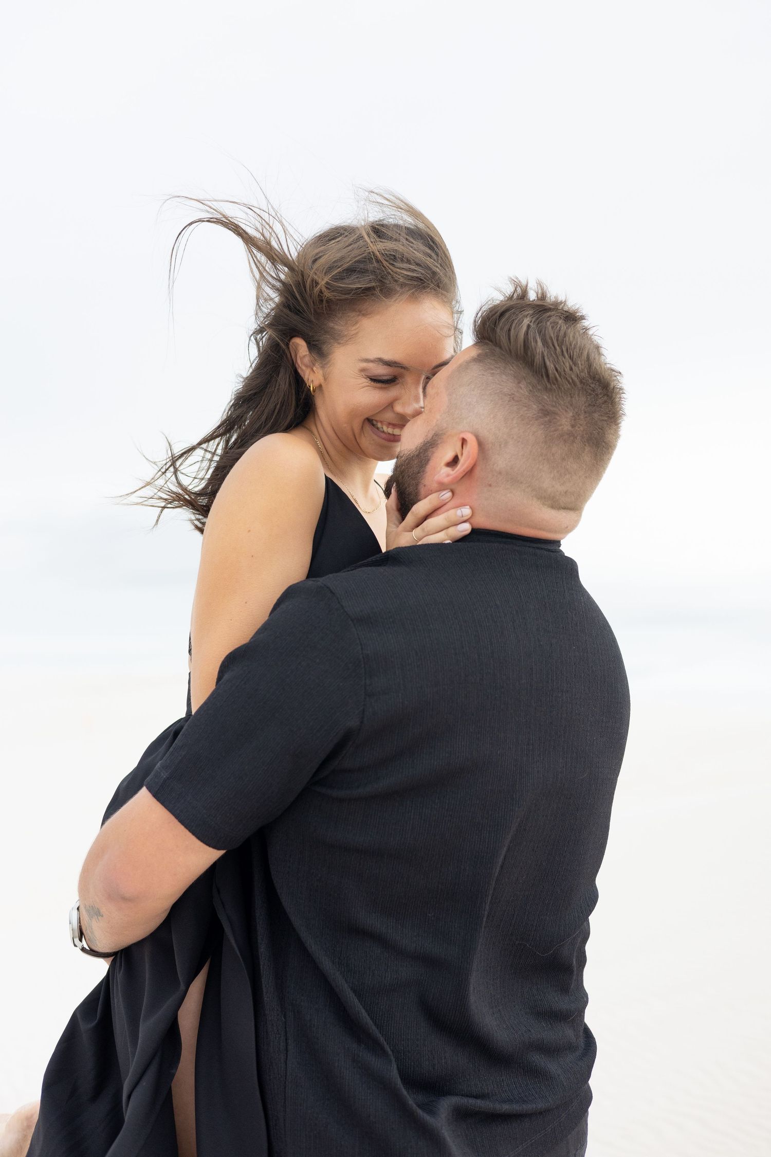 Romantic couple embracing and laughing together on white sandy beach.