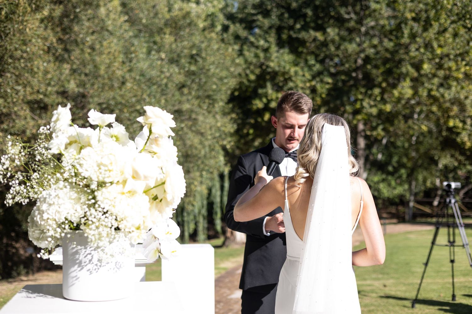 Outdoor wedding ceremony with white floral arrangements and natural garden setting.