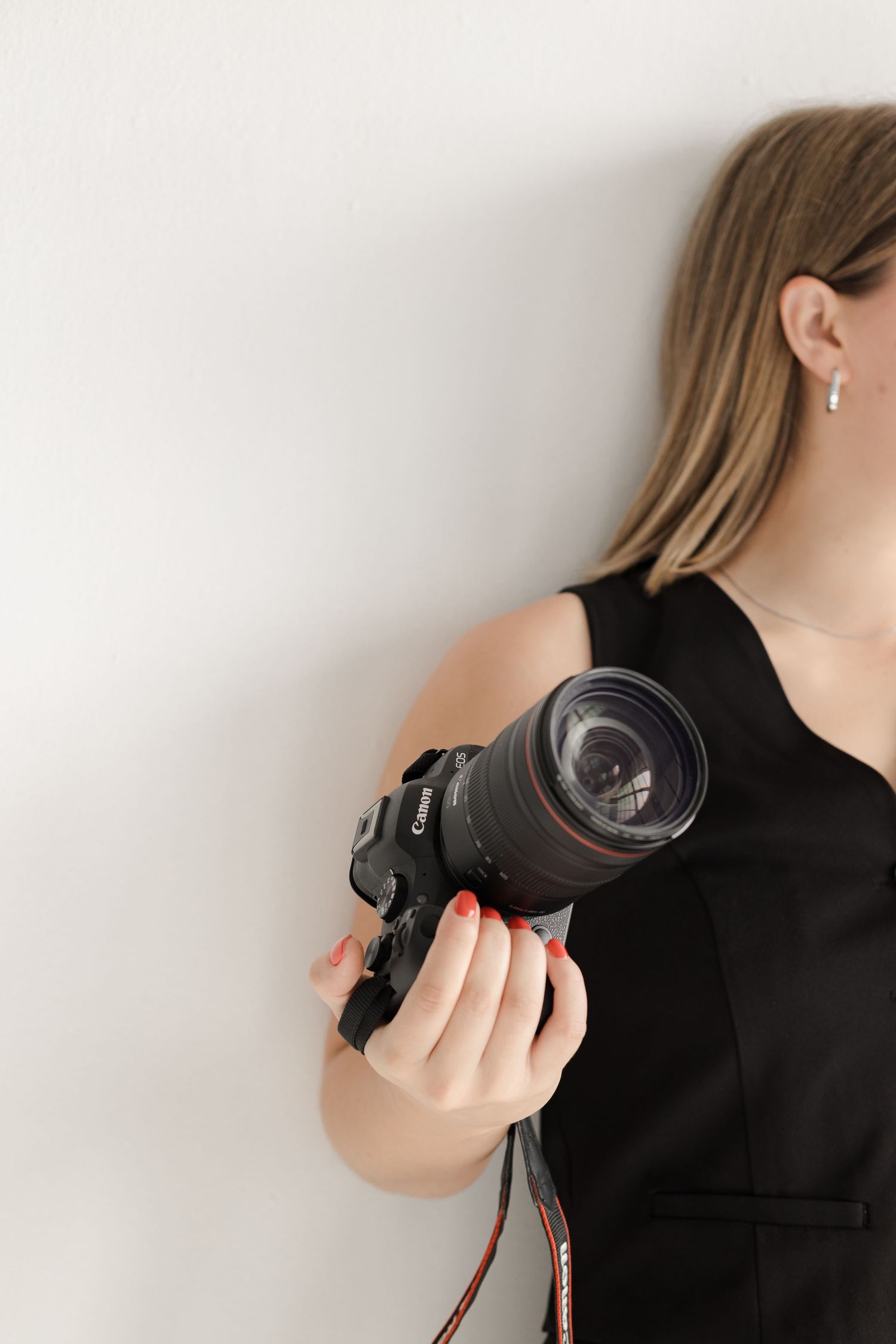 Close-up of photographer holding professional camera lens against white wall.