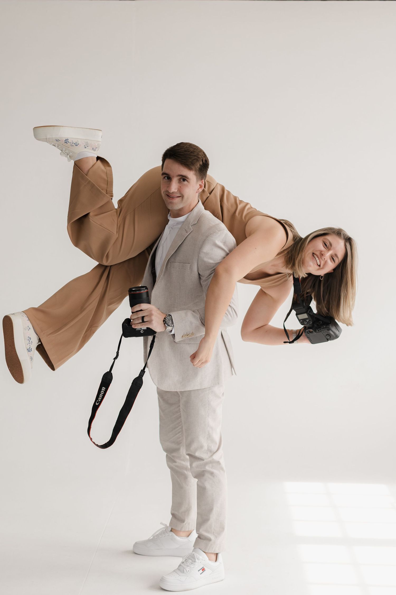 Creative photography duo pose playfully with cameras in modern studio setting.