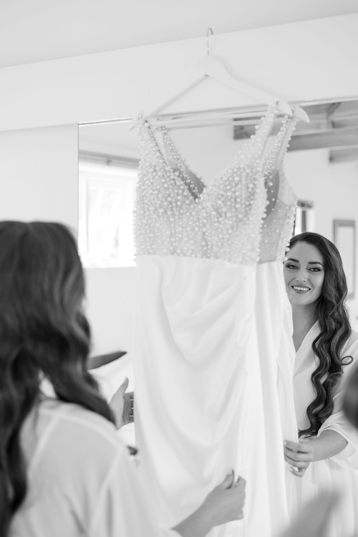 A white wedding dress with beaded bodice hangs on display as reflections appear in a mirror.