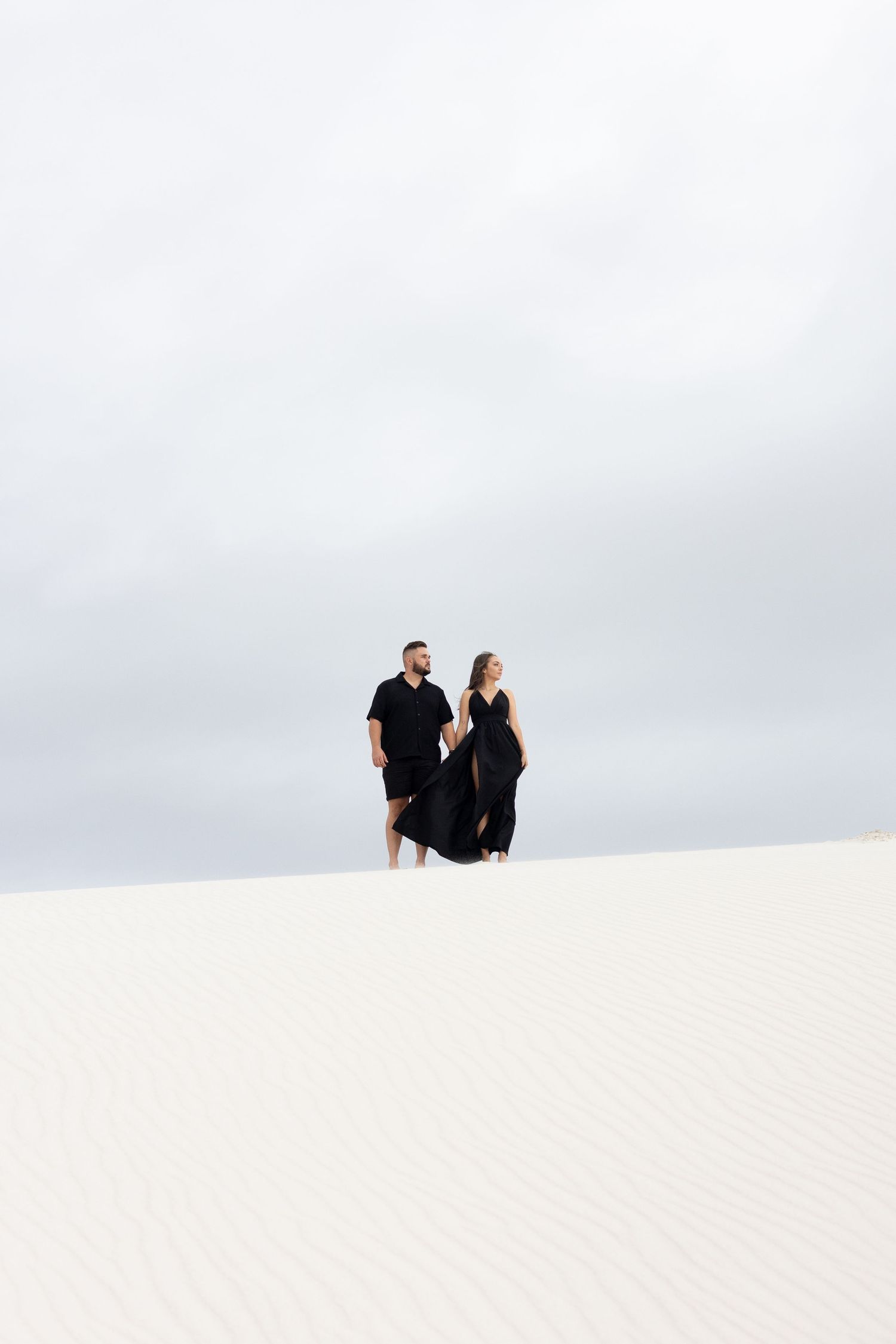 Distant silhouette of couple in black standing together on bright white sand dunes.
