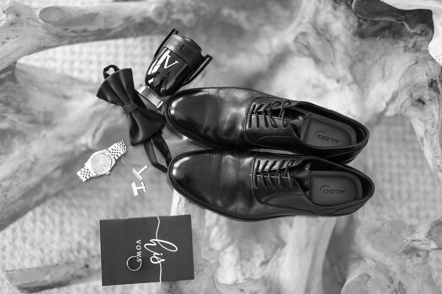 Classic black leather groom's shoes with bow tie on textured surface.