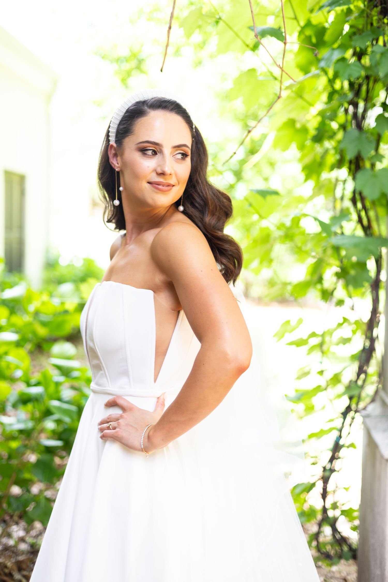 A woman in an elegant white strapless wedding gown poses outdoors against a backdrop of lush green foliage.