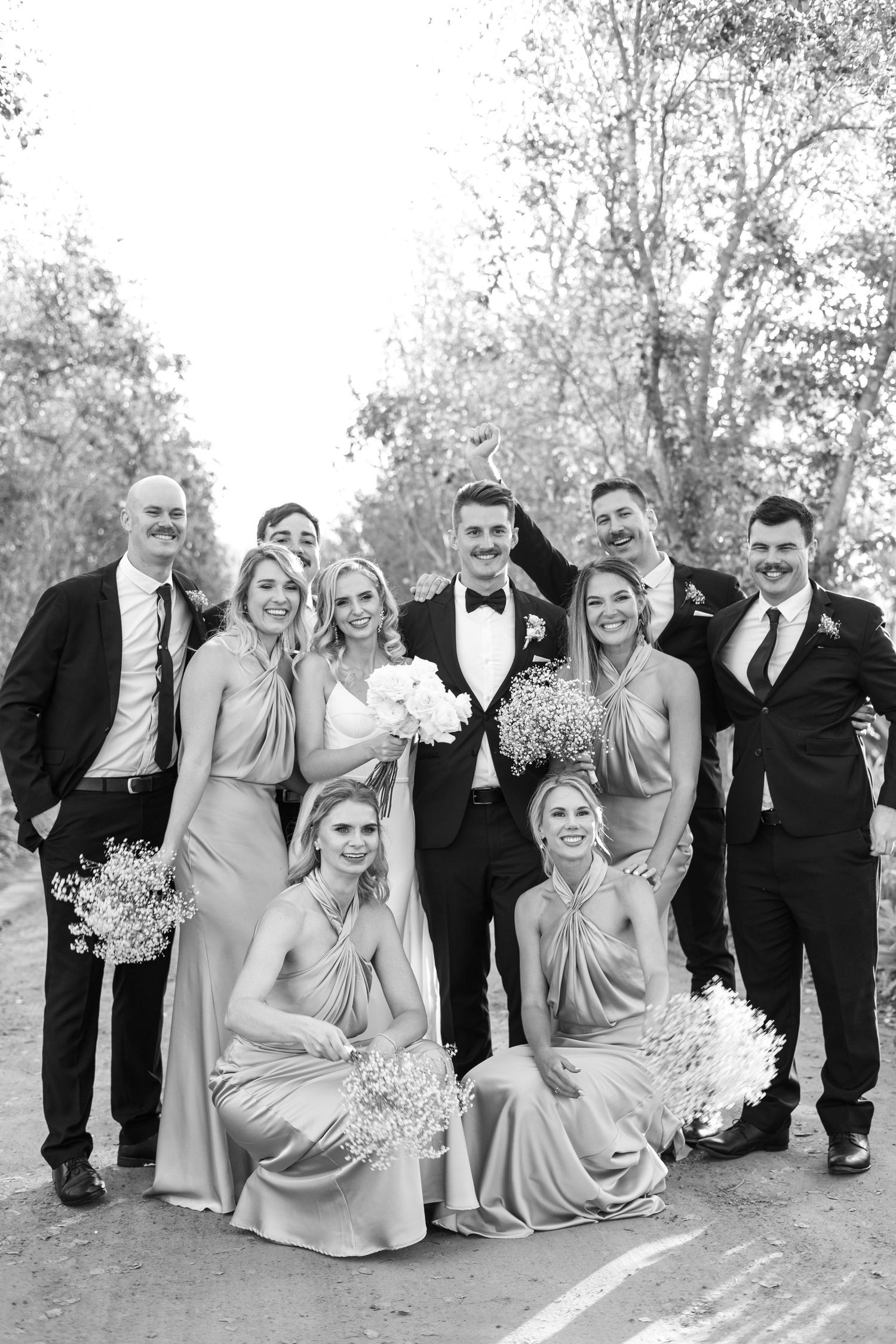 Black and white portrait of wedding party in formal attire on outdoor path.