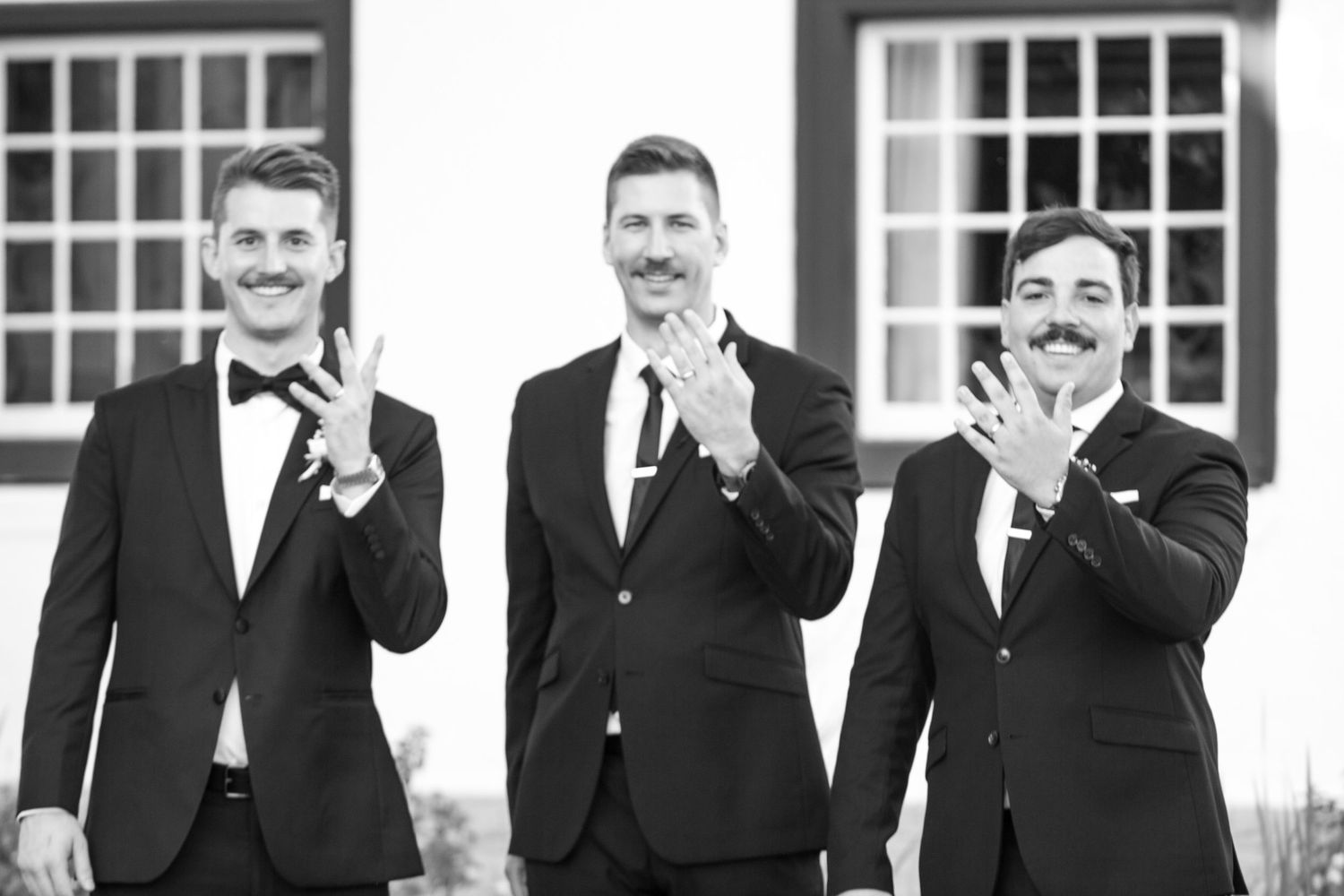 Three groomsmen in black tuxedos laughing and gesturing together.