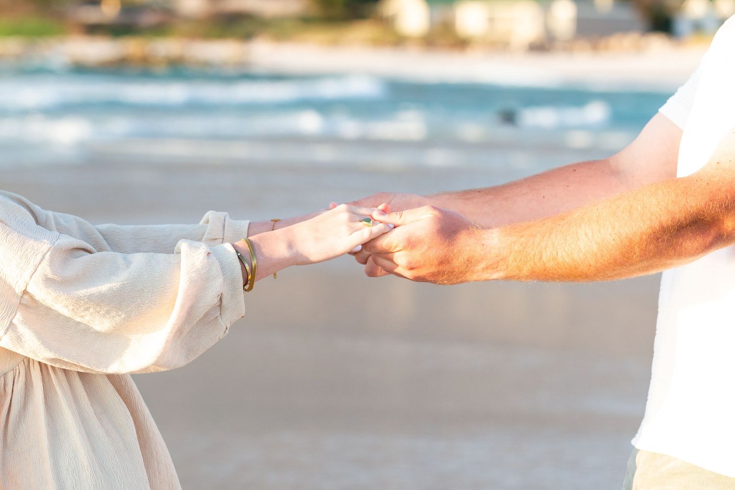 Close-up of couple holding hands on sunny beach.