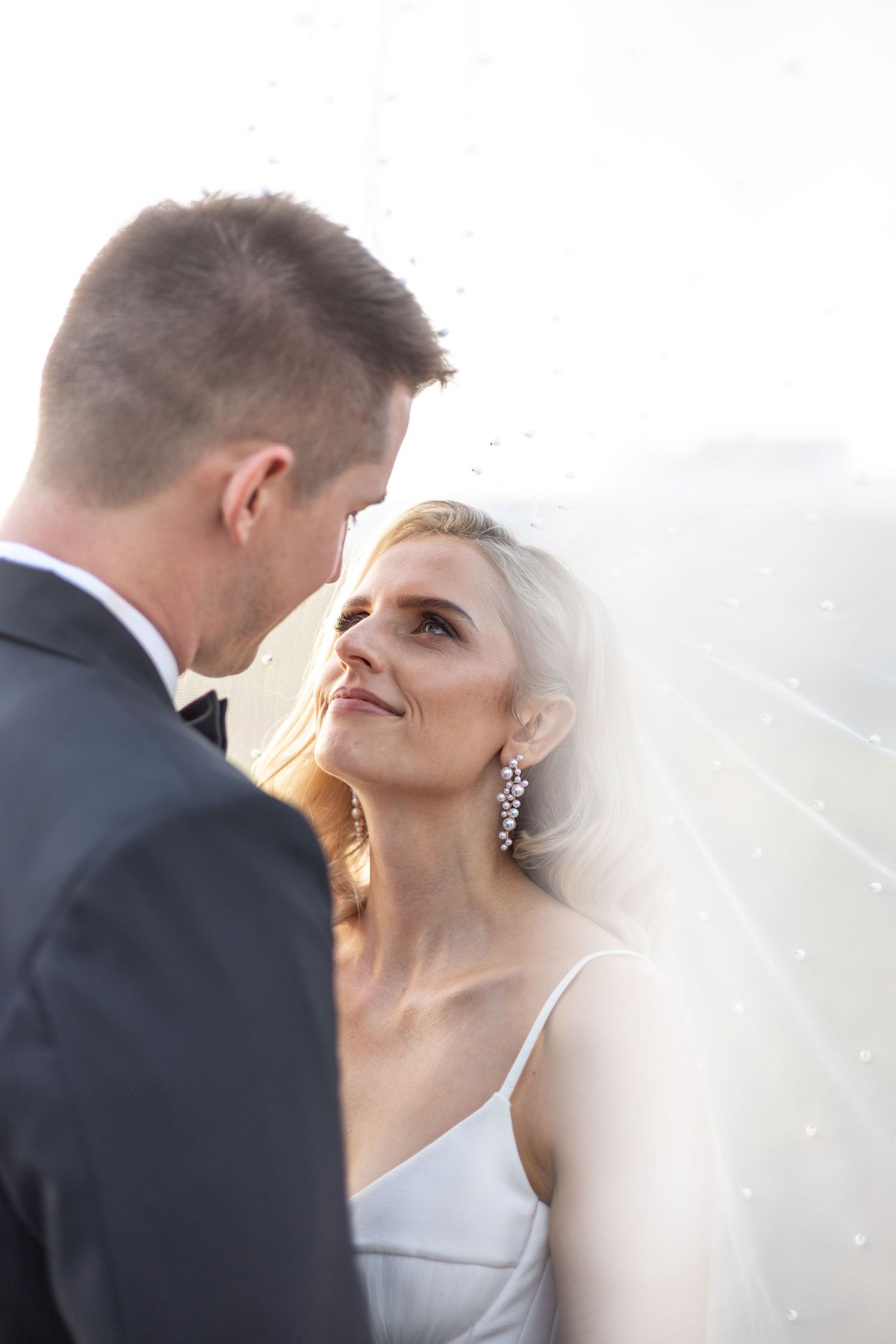 Bride and groom share an intimate moment outdoors during golden hour with her veil flowing in the breeze.
