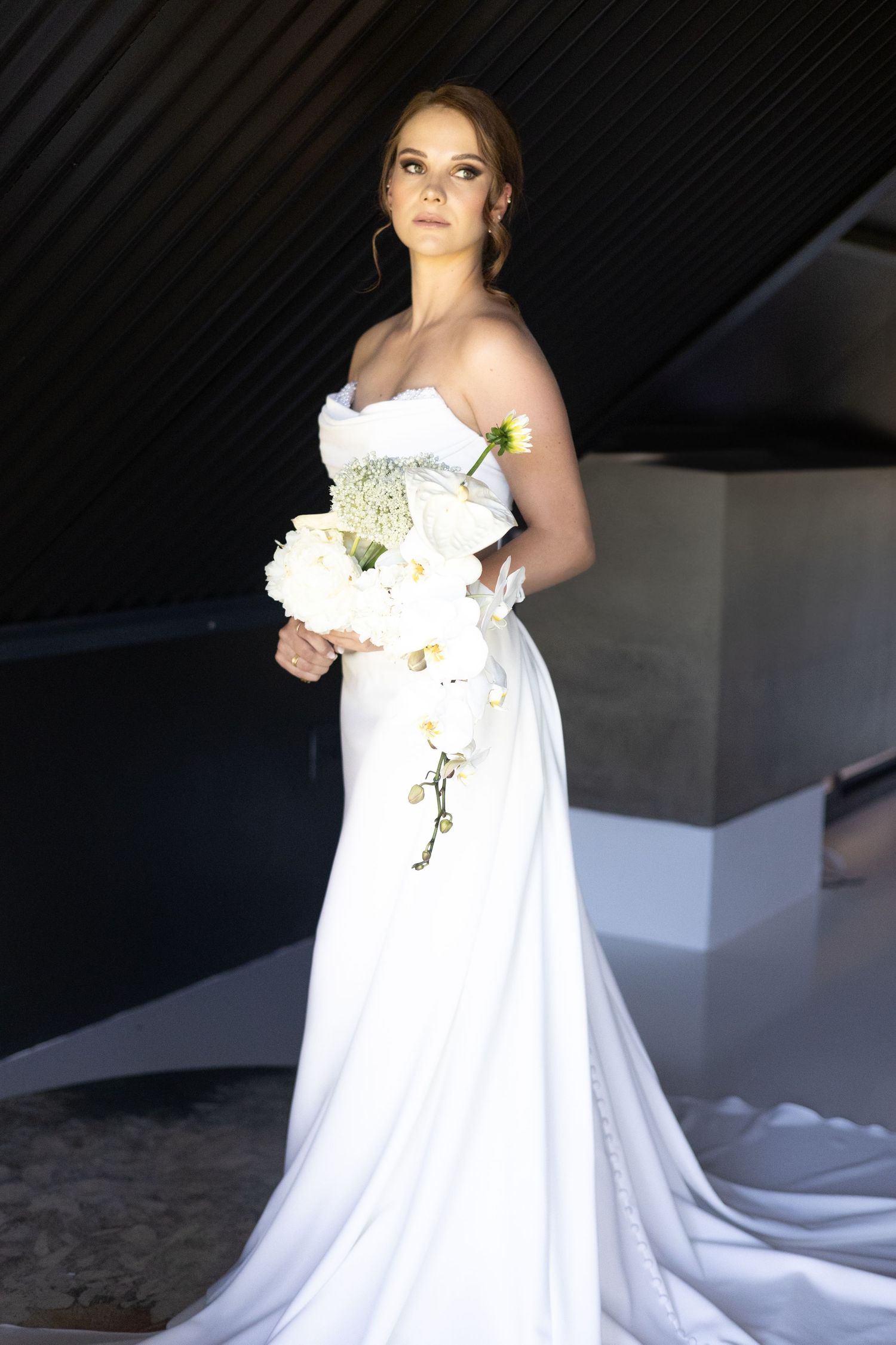 An elegant white wedding gown with a strapless design and flowing train is showcased in a dramatic light.