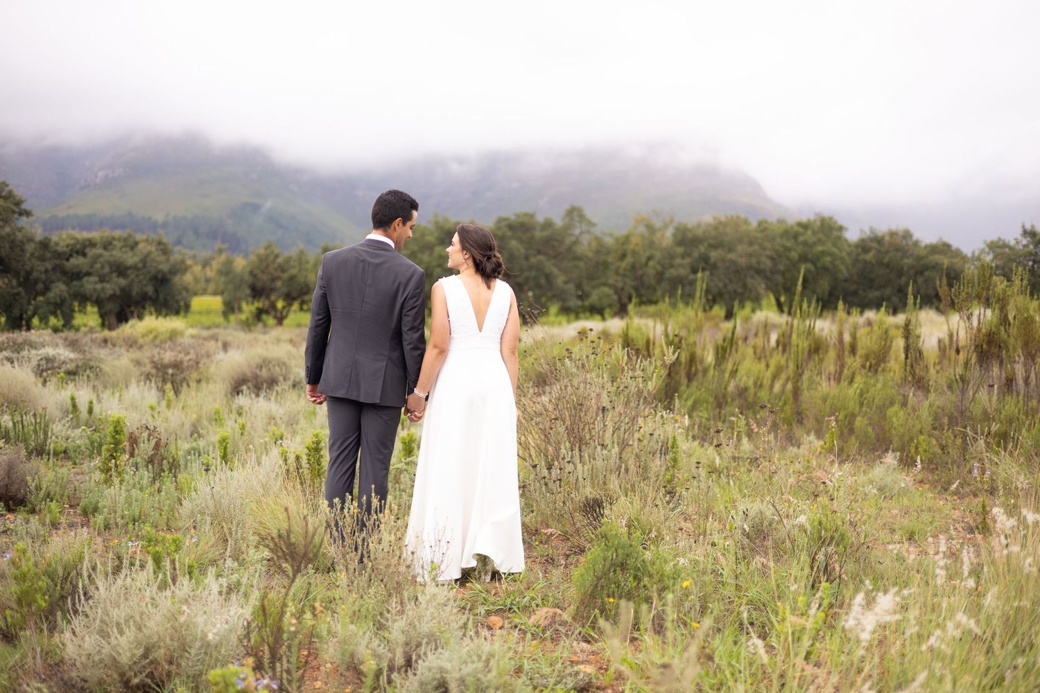 Couple in wedding attire standing together in a scenic mountain landscape with desert brush.