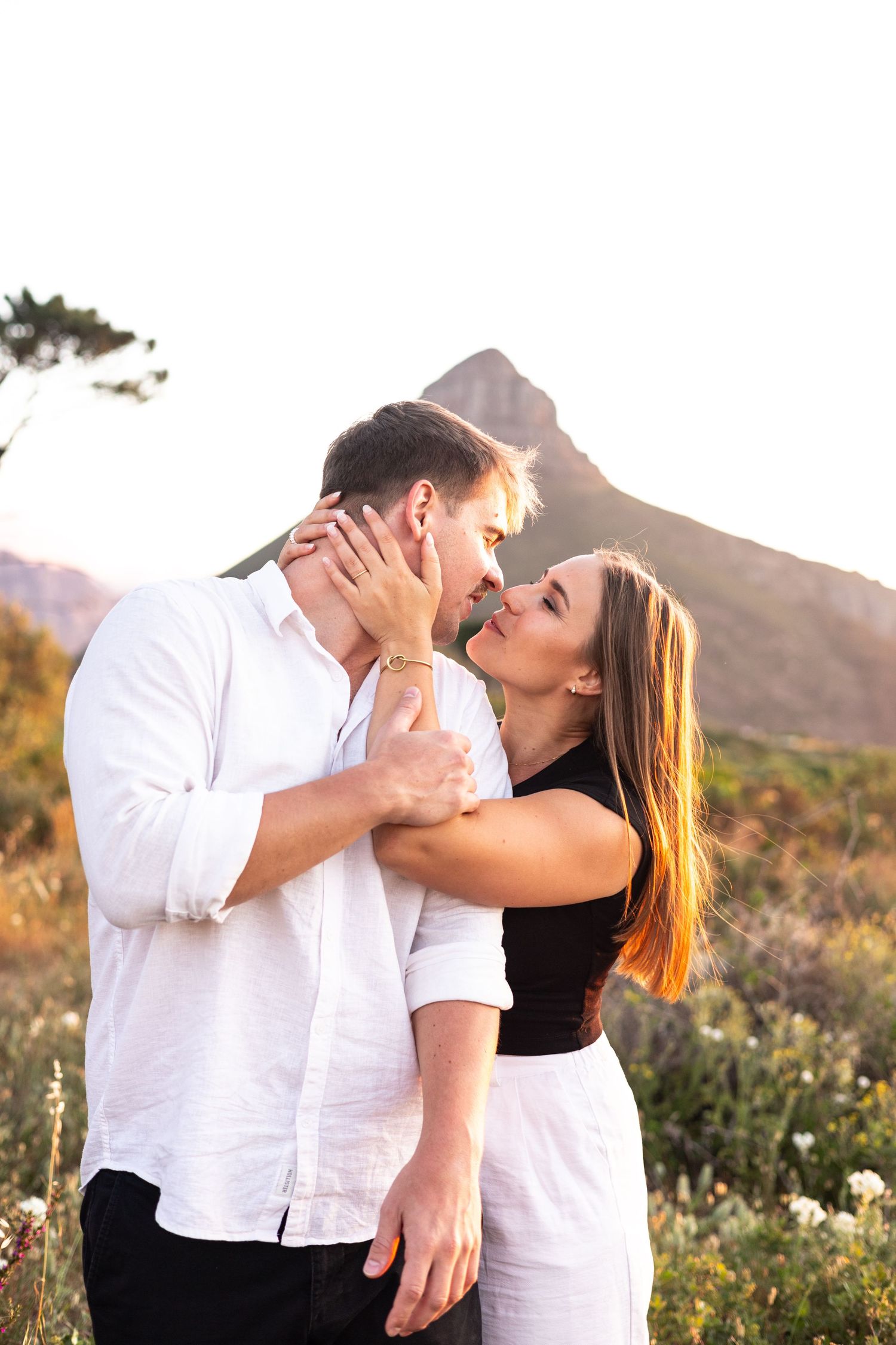 Romantic couple sharing intimate moment against mountain landscape at sunset.