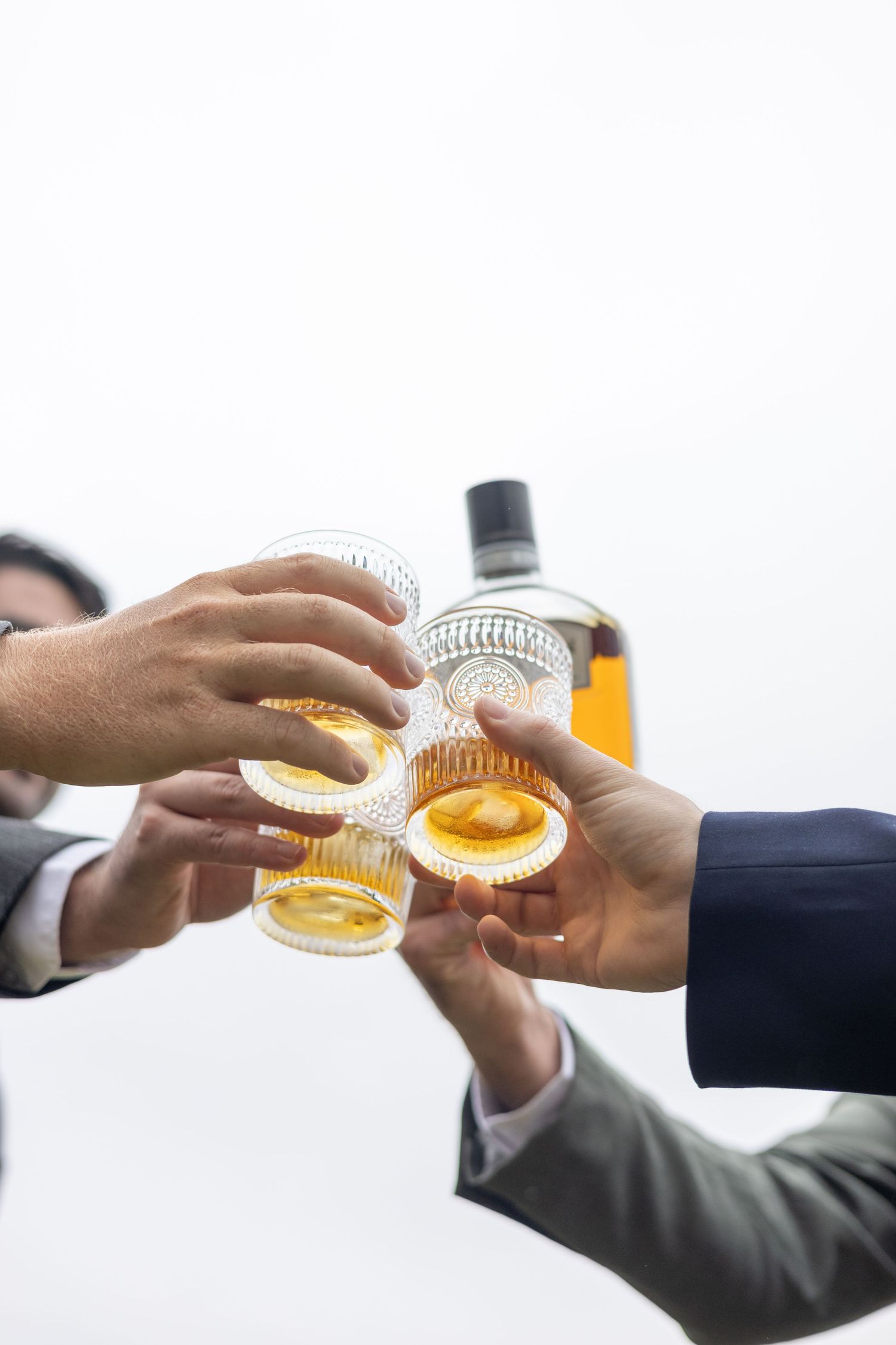 Close-up sequence of hands toasting with glasses of whiskey or bourbon in a celebratory moment.