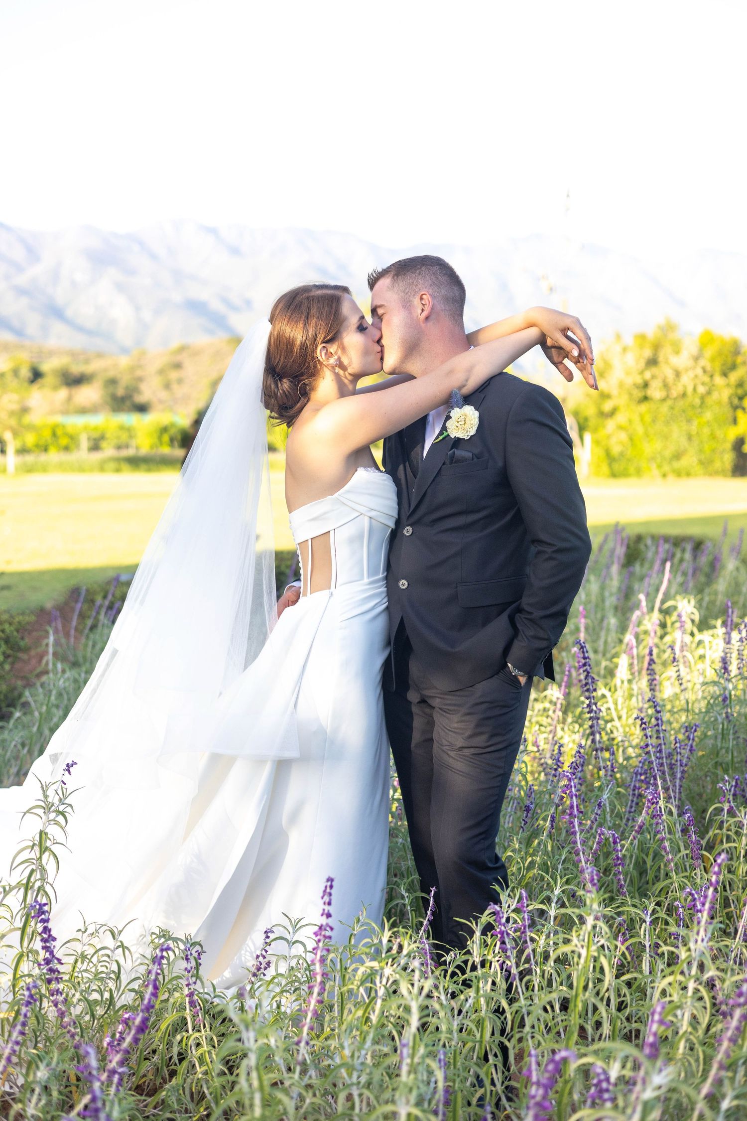 Newlyweds embrace in a meadow of purple wildflowers during a golden hour outdoor wedding photoshoot.