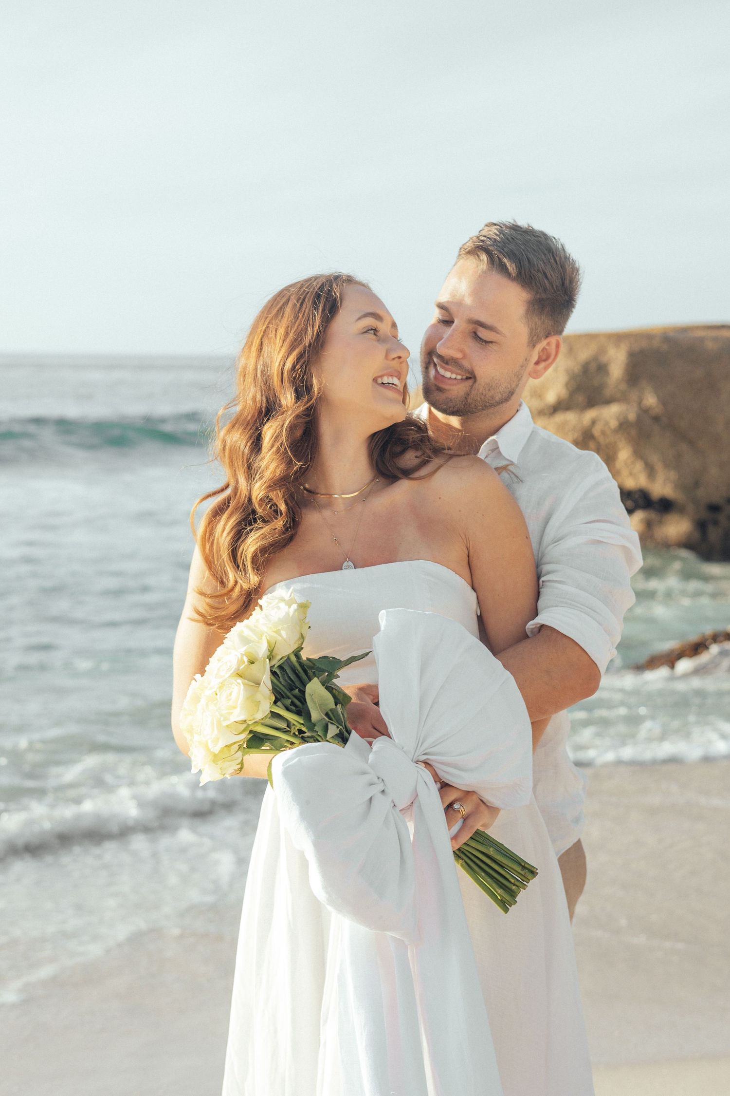 Romantic beach wedding couple embracing near ocean cliffs at golden hour.
