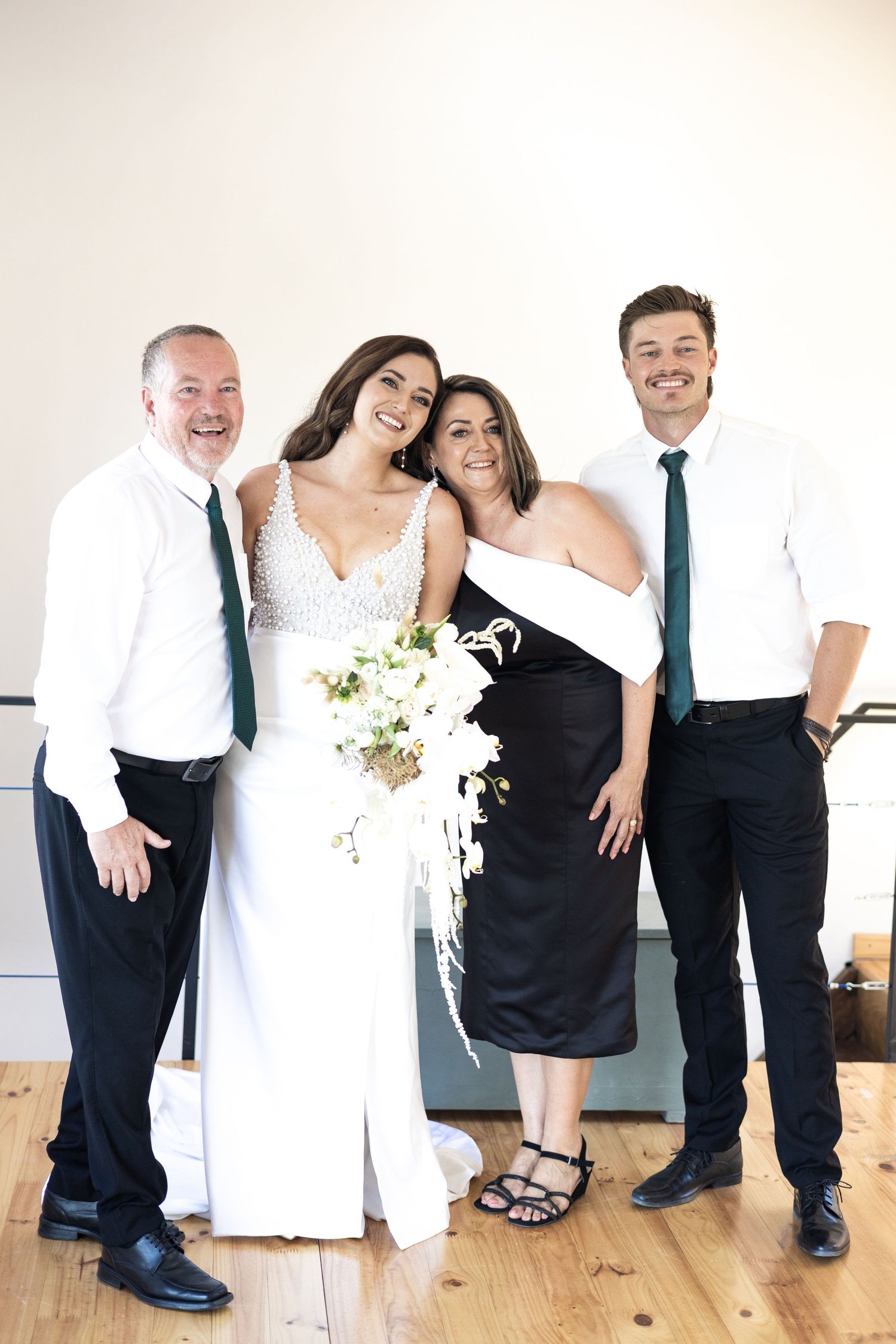 Wedding party group poses together indoors wearing elegant black and white formal attire, with white floral bouquet.