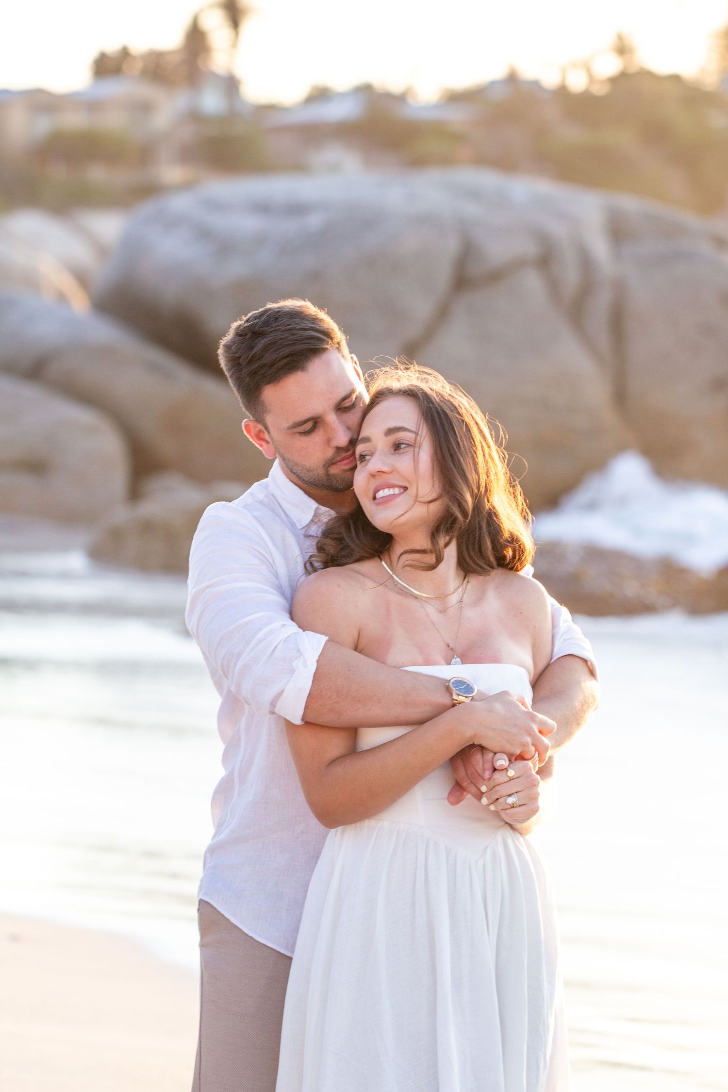 Intimate couple's portrait at sunset on rocky beach in wedding attire.