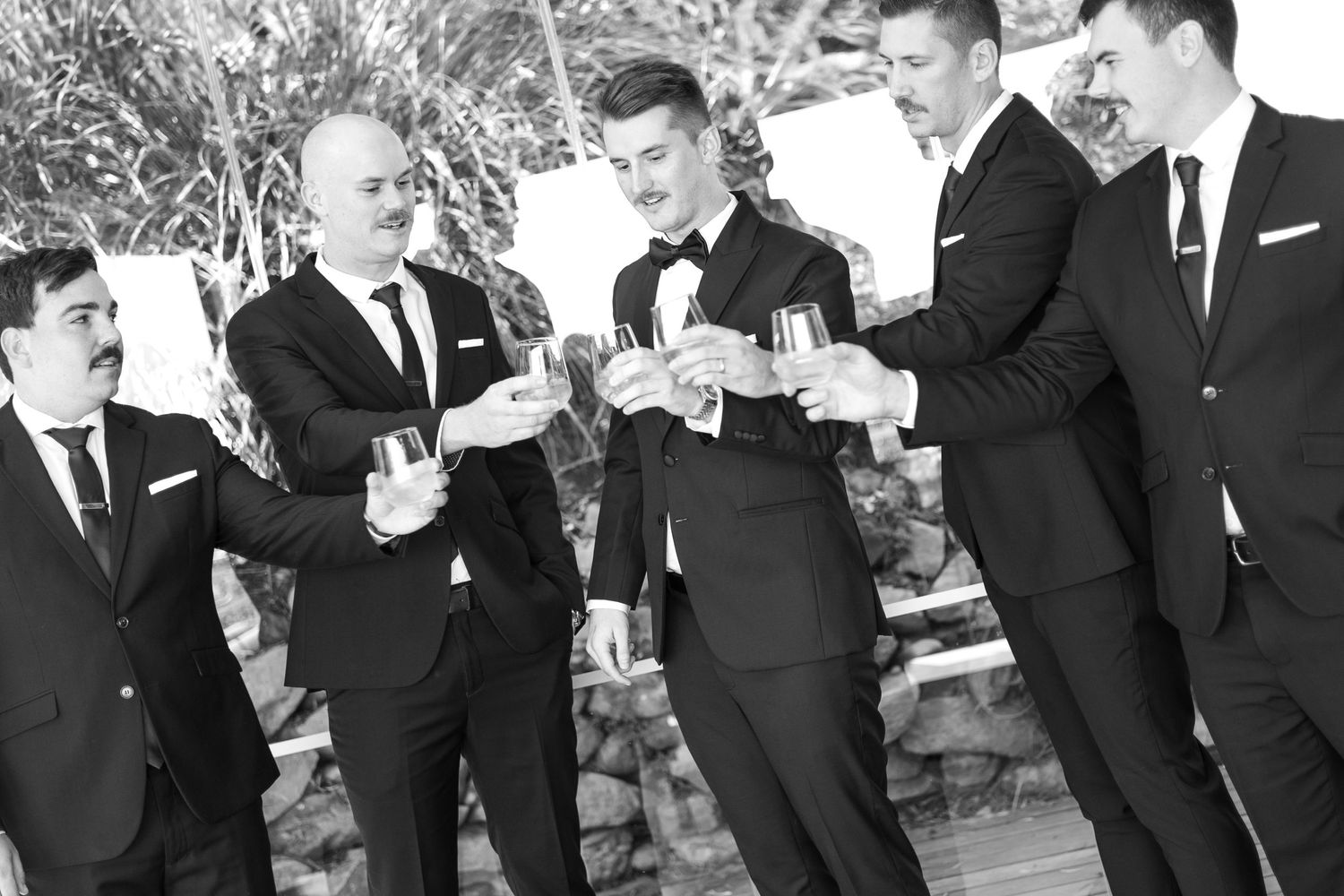 Groomsmen in formal suits checking their phones together outdoors.
