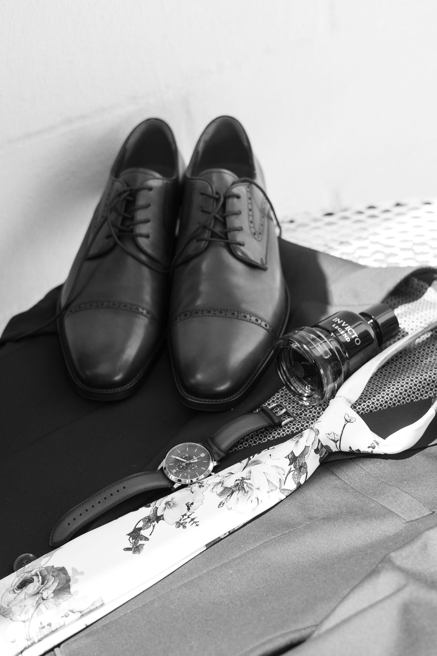 Black leather dress shoes with a tie placed on dark surface in a black and white photograph.