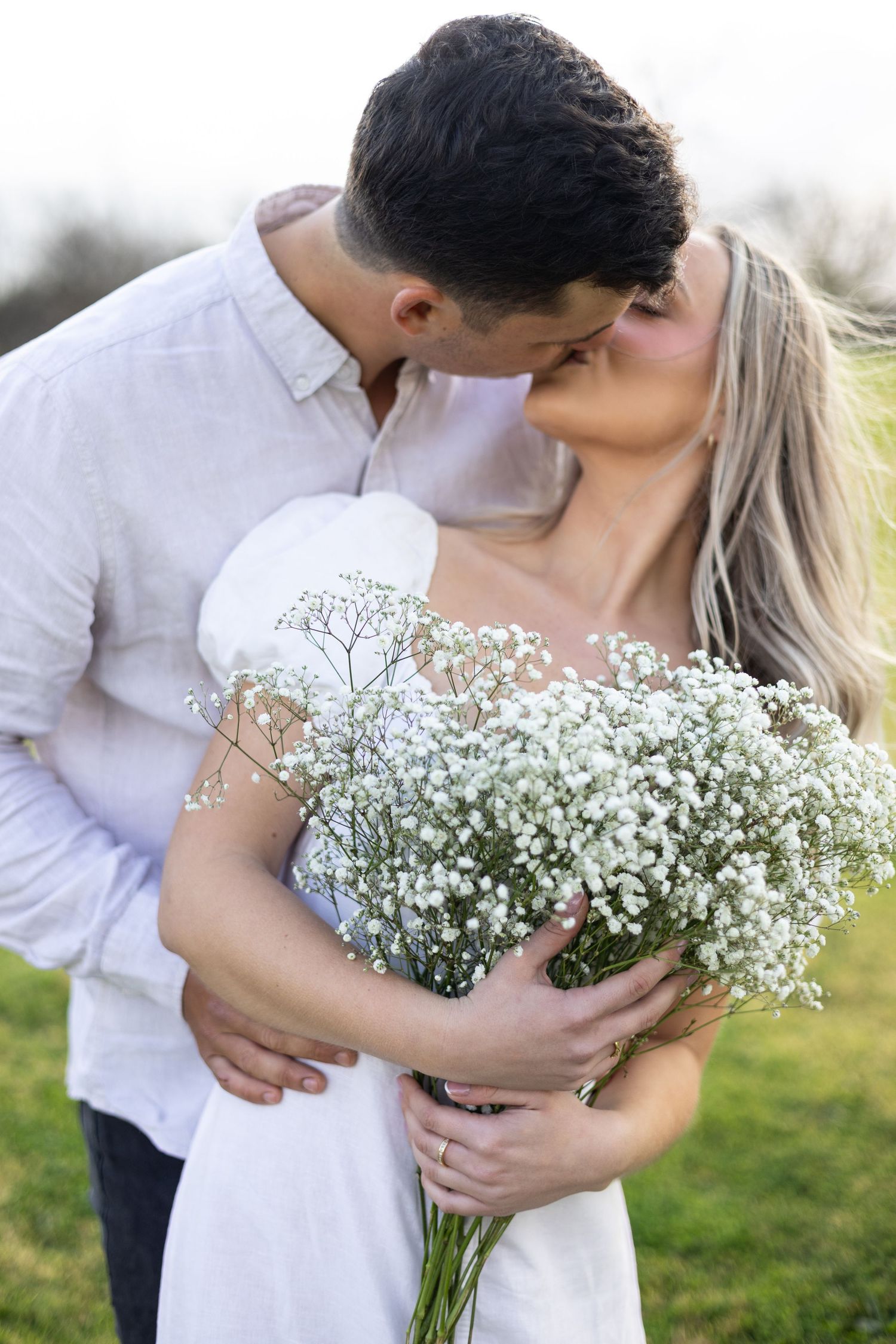 Romantic couple sharing intimate moment with baby's breath bouquet in countryside setting.