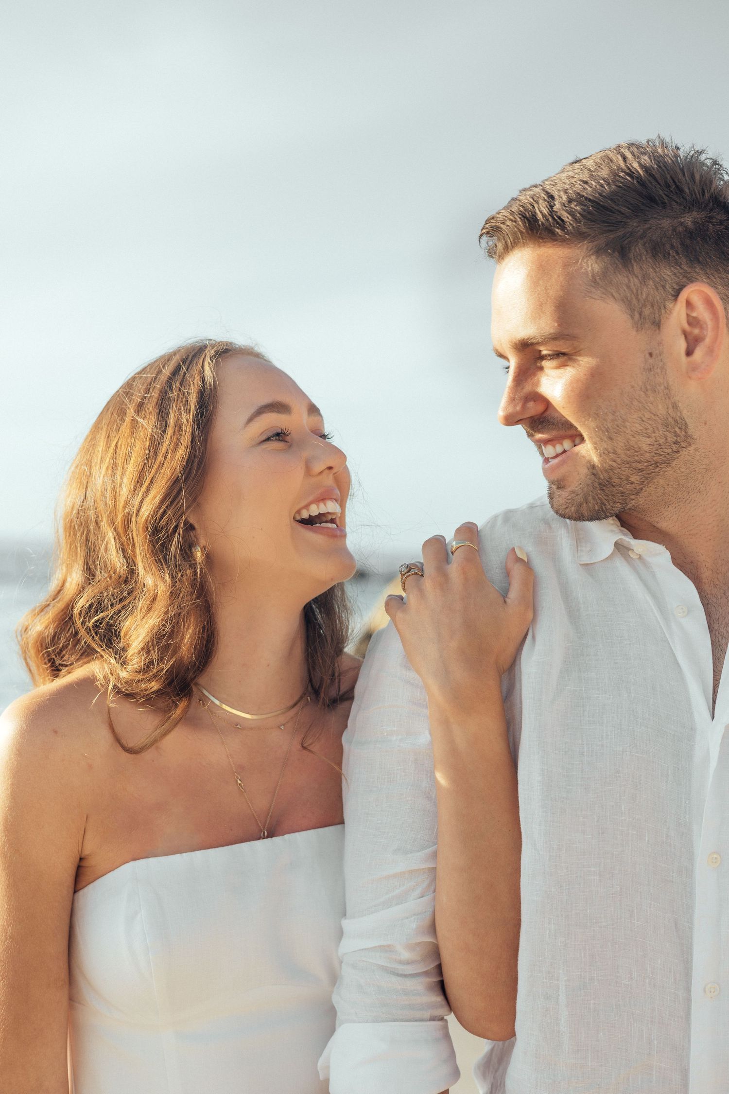 Couple shares joyful laughter in intimate moment on sunny beach.