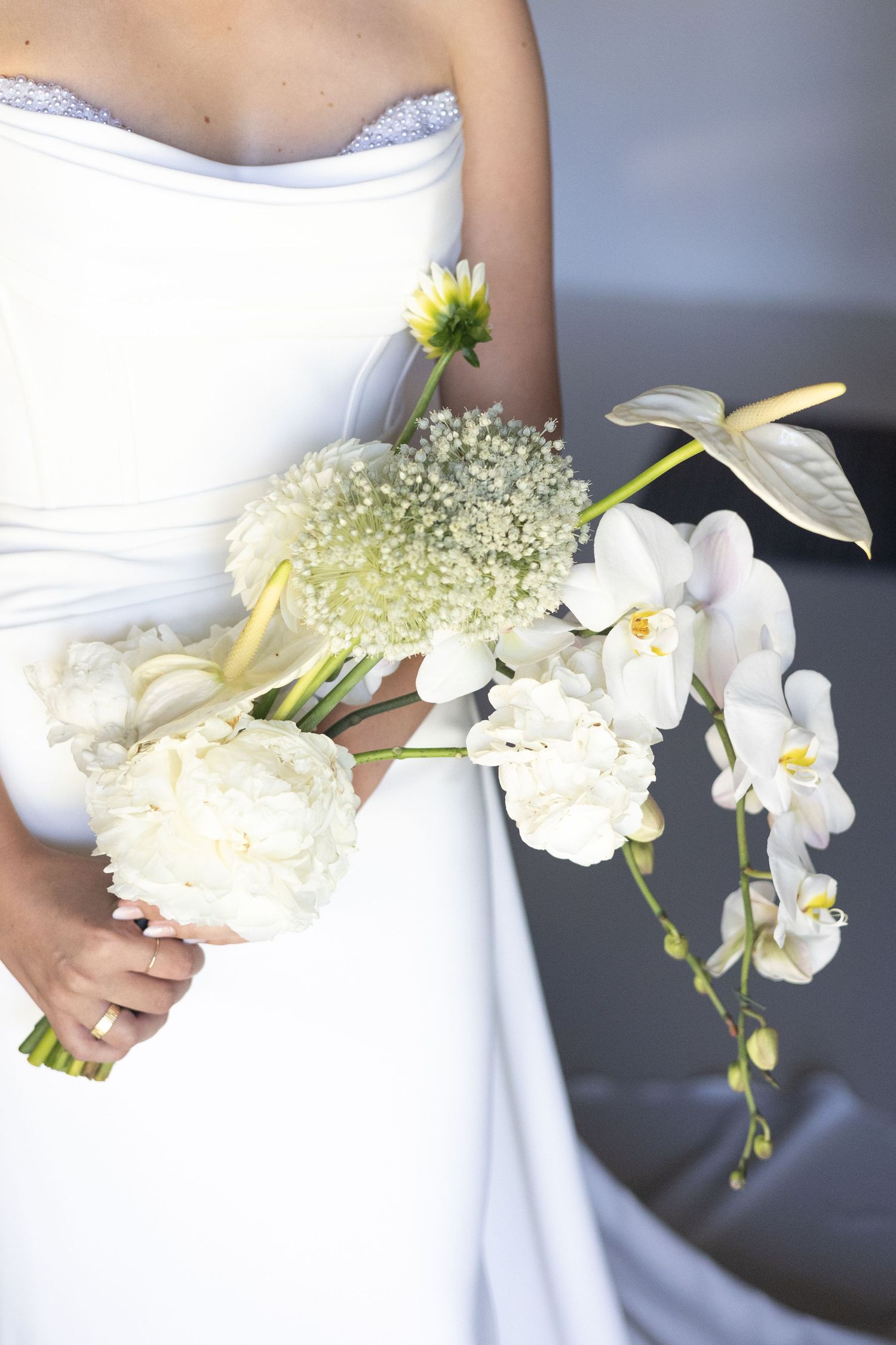 White orchids and peonies in an elegant bridal bouquet against a white wedding dress.